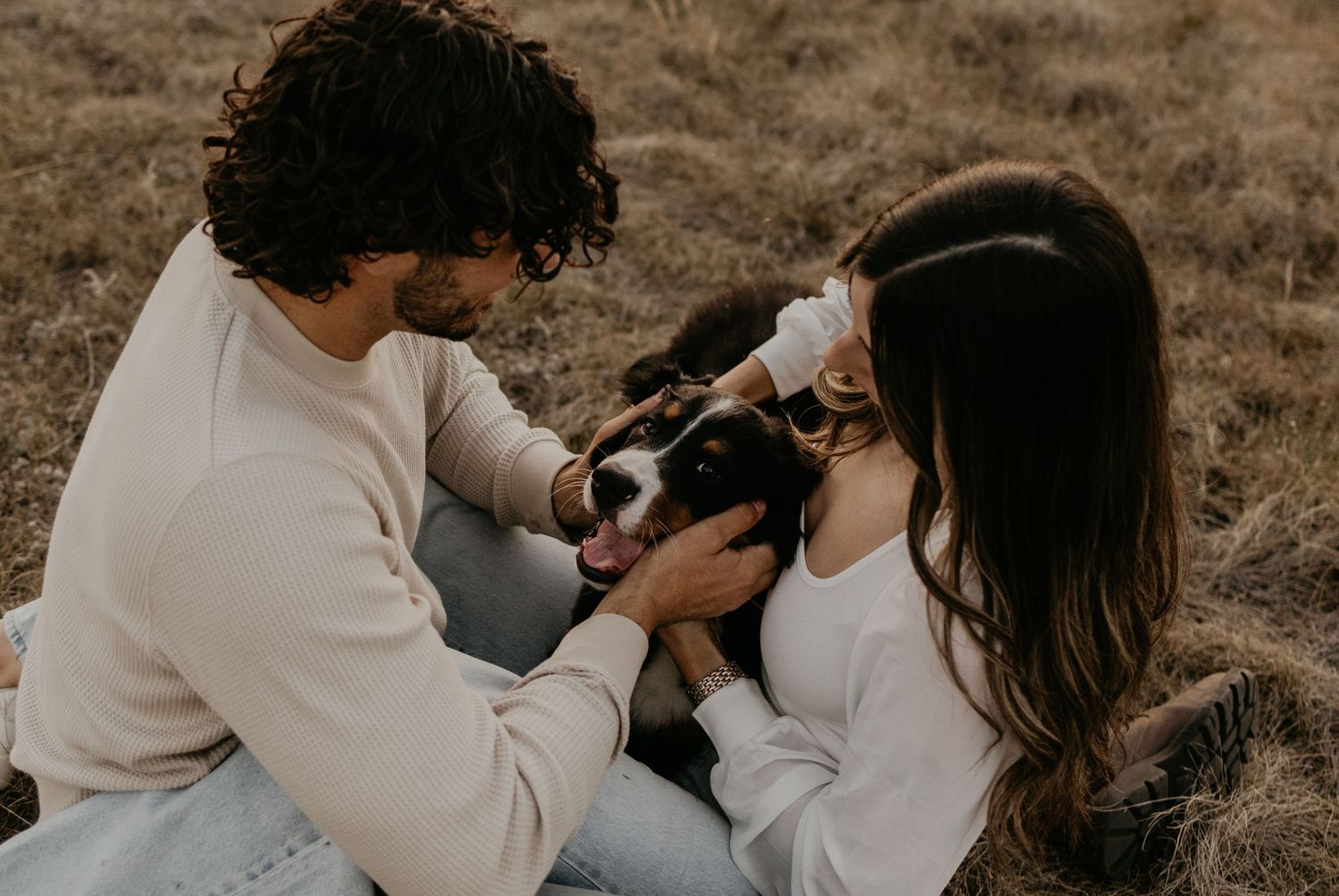 Couple holding dog in outdoor setting with natural lighting.
