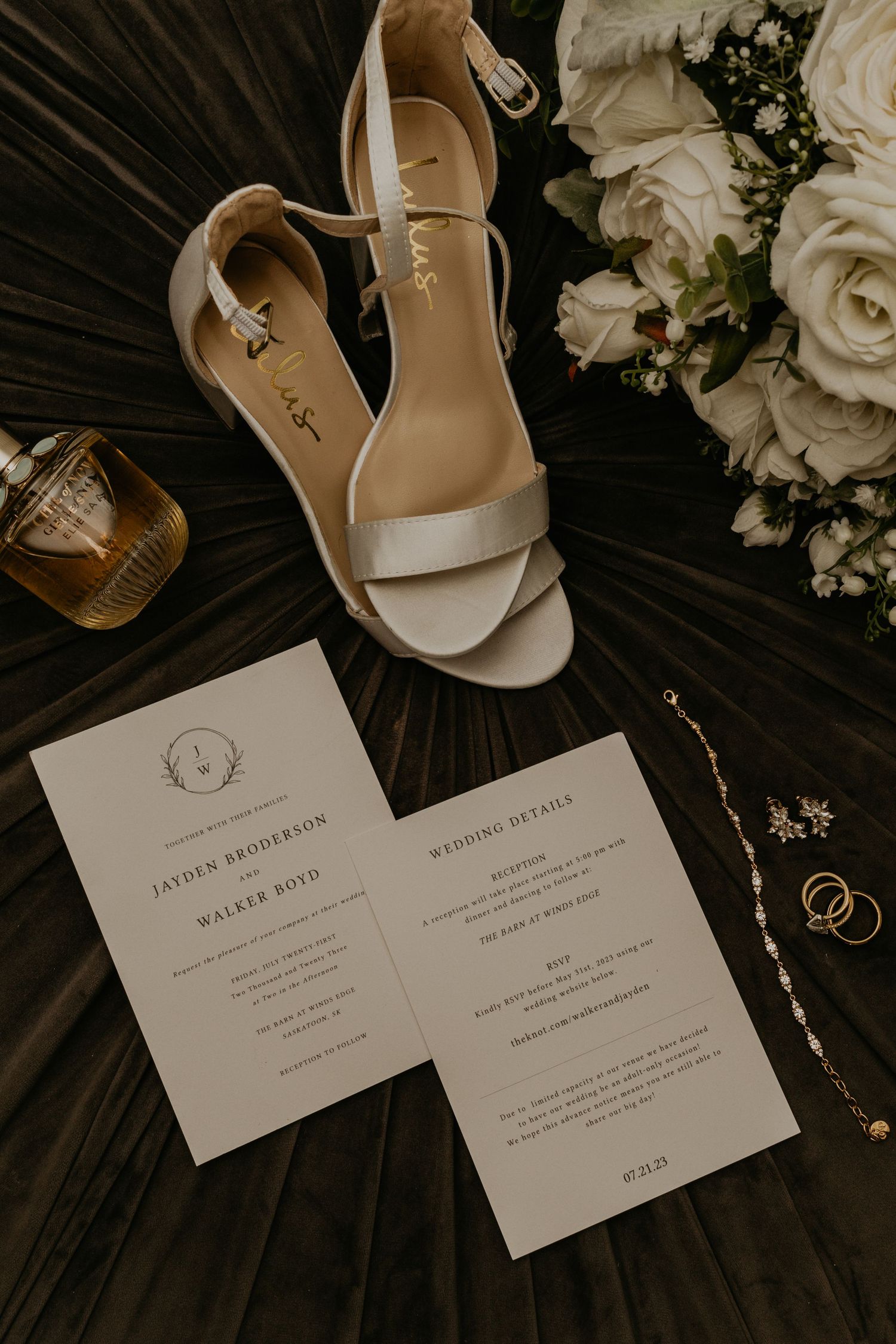 Wedding invitation cards with white heels and roses on dark surface.