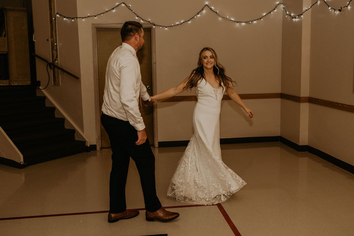 Wedding couple dancing on reception floor decorated with string lights.