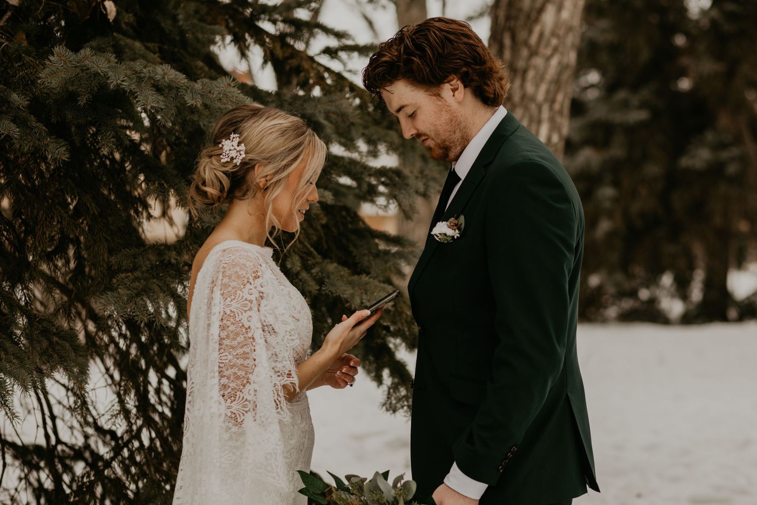 A winter wedding moment shared between a couple next to snow-covered evergreen trees.
