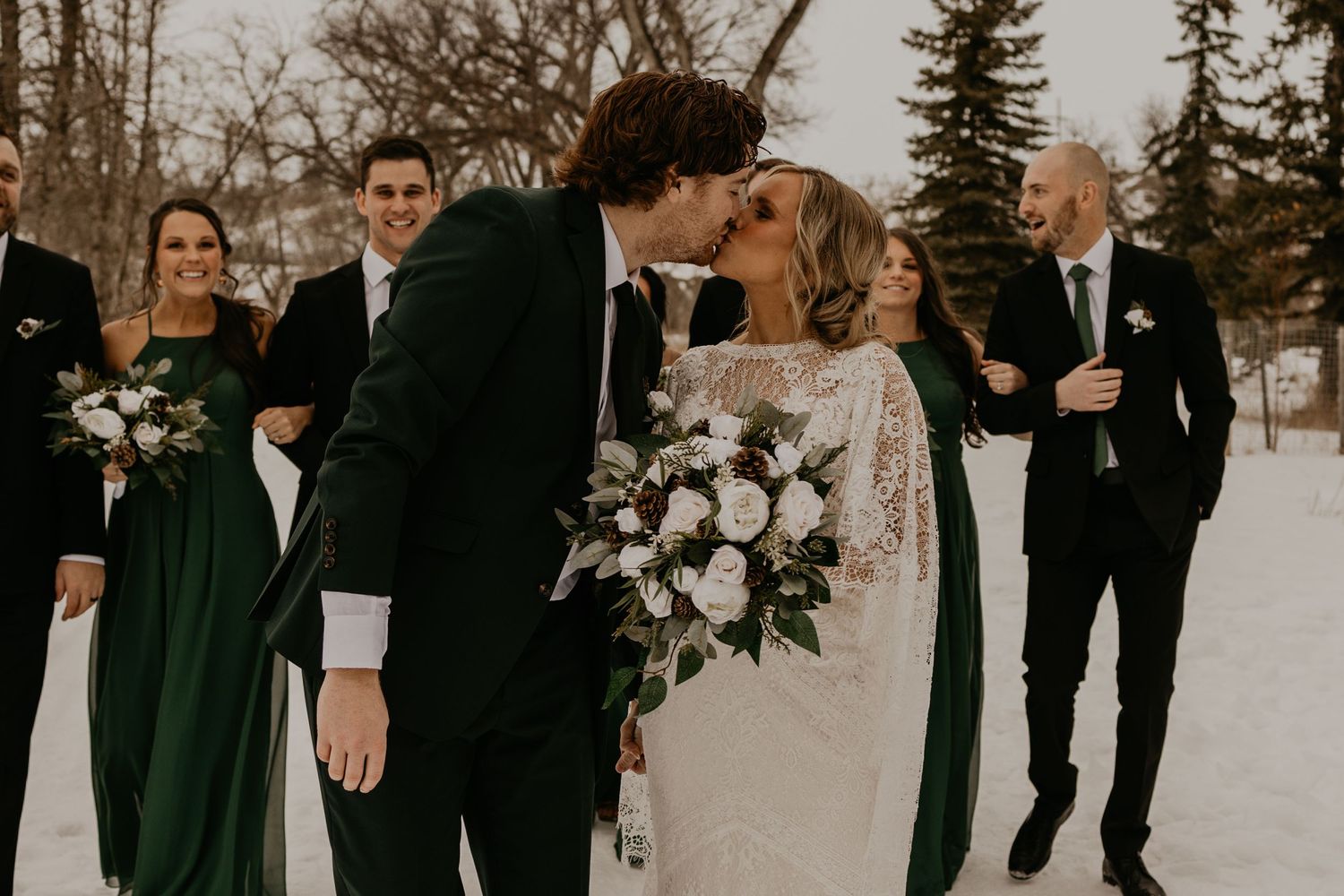 Candid moment of wedding party on snowy winter day with forest backdrop.