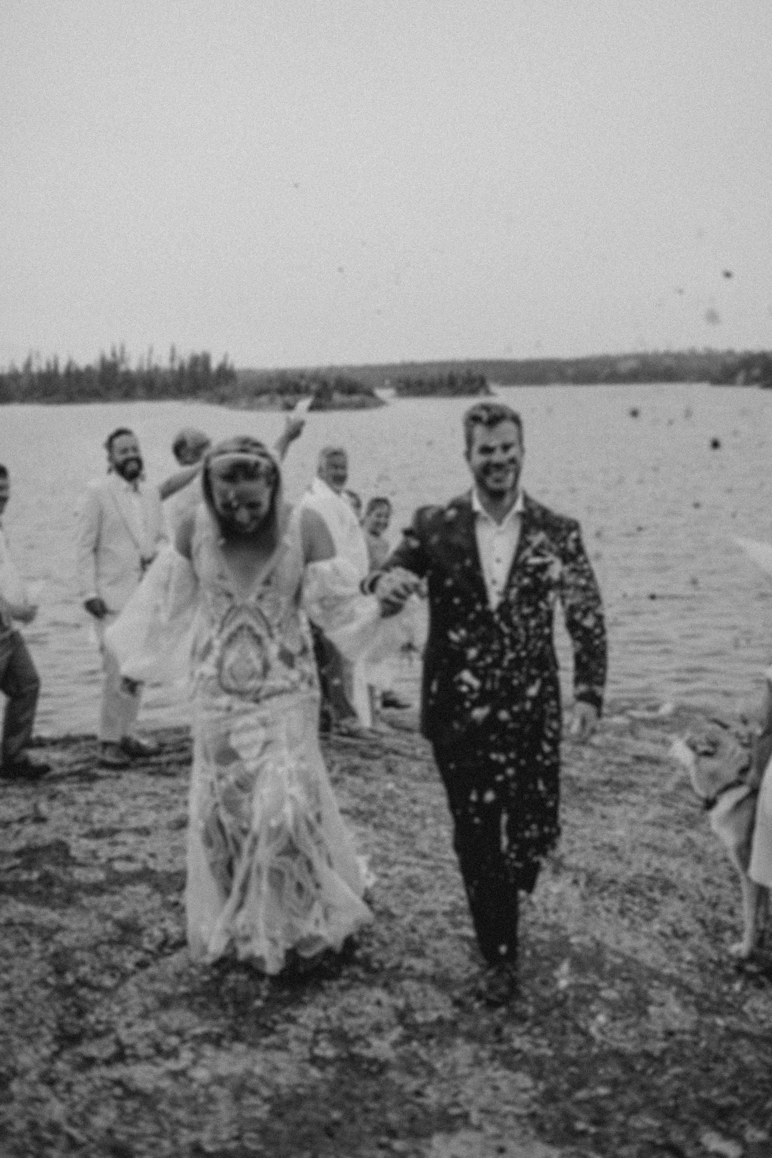 A vintage black and white lakeside wedding photo showing a couple walking along the shoreline in wedding attire.