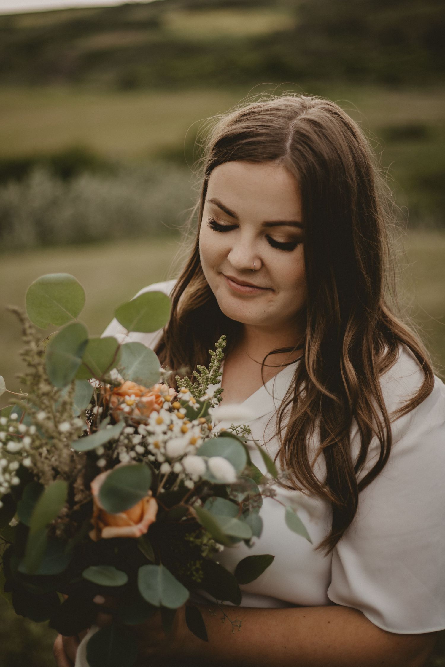 Woman holding rustic bouquet with eucalyptus and wildflowers smiles softly.