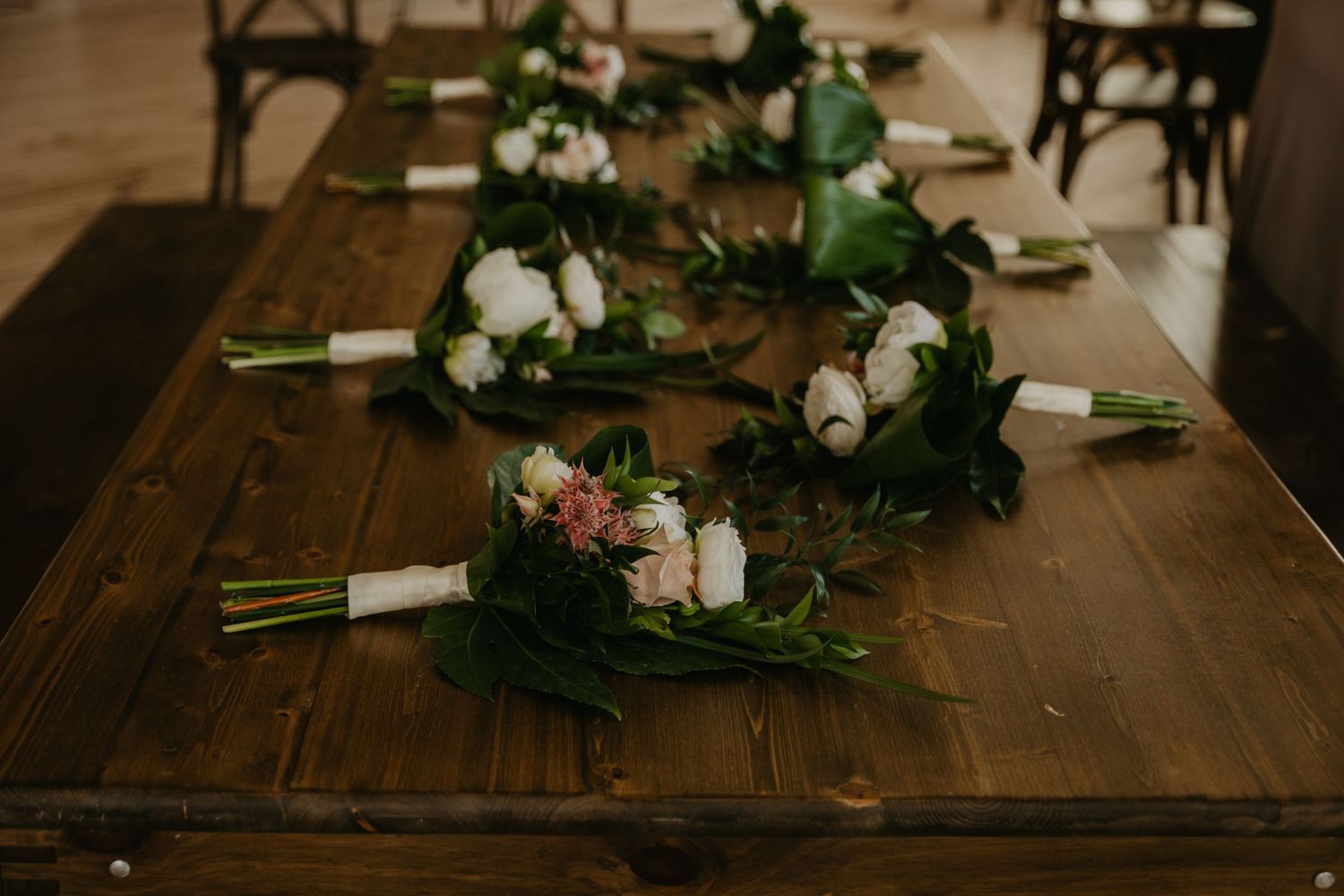 Wedding bouquets with white flowers and greenery arranged on a wooden table.