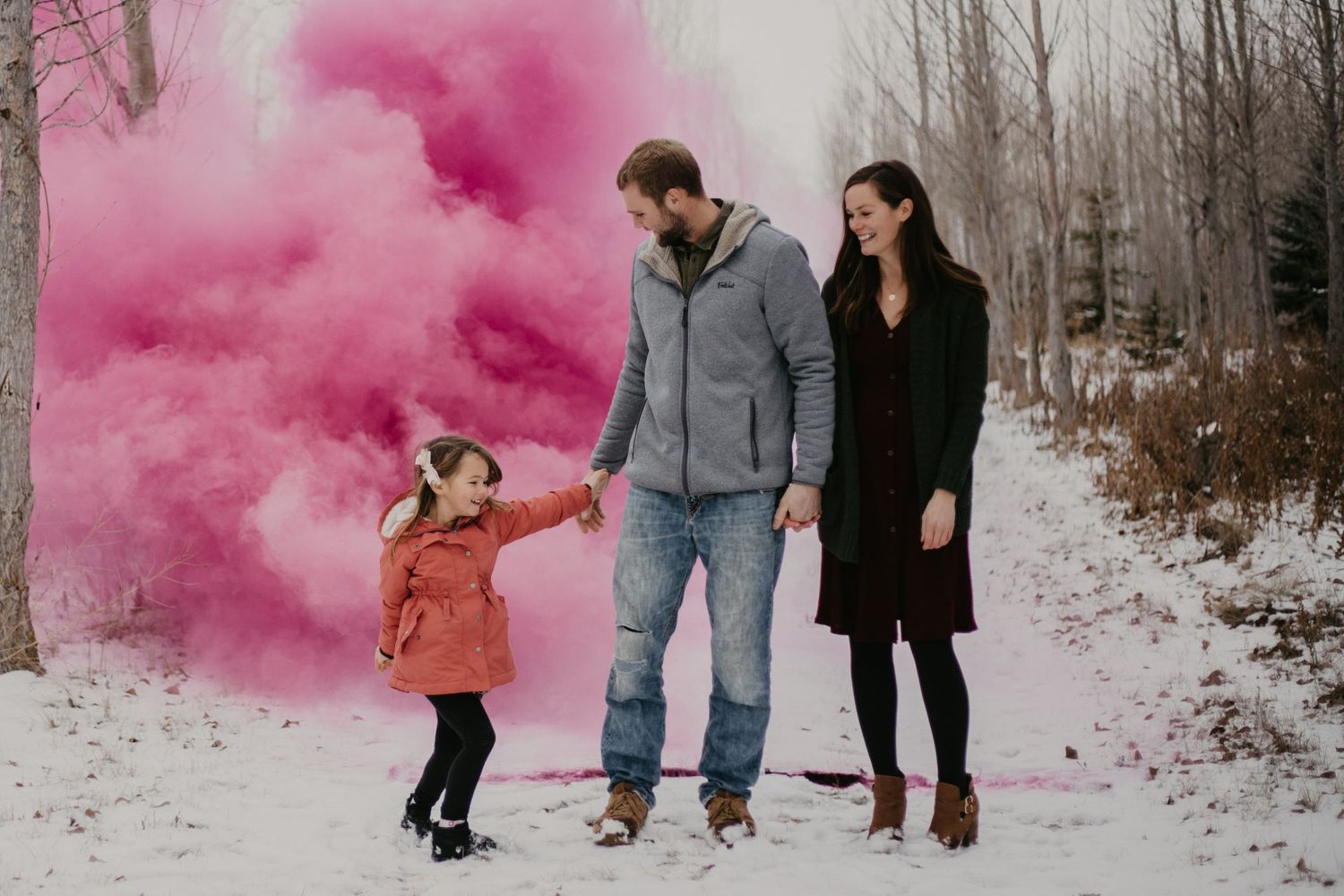 A family enjoys a winter photo session with vibrant pink smoke effects in the snow.