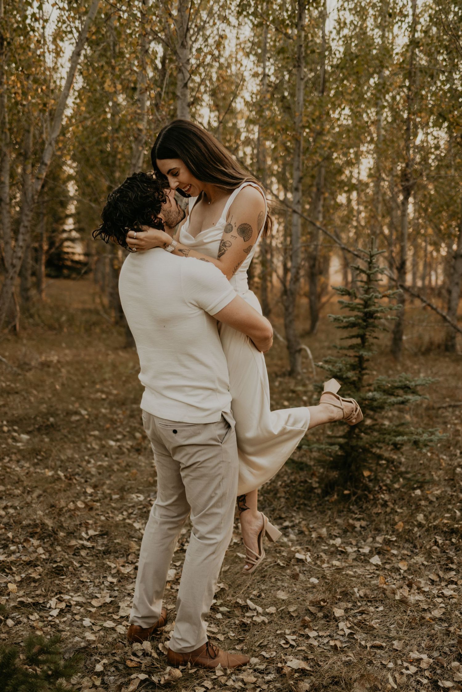 A romantic autumn engagement photo shows a couple embracing in a grove of golden aspen trees.