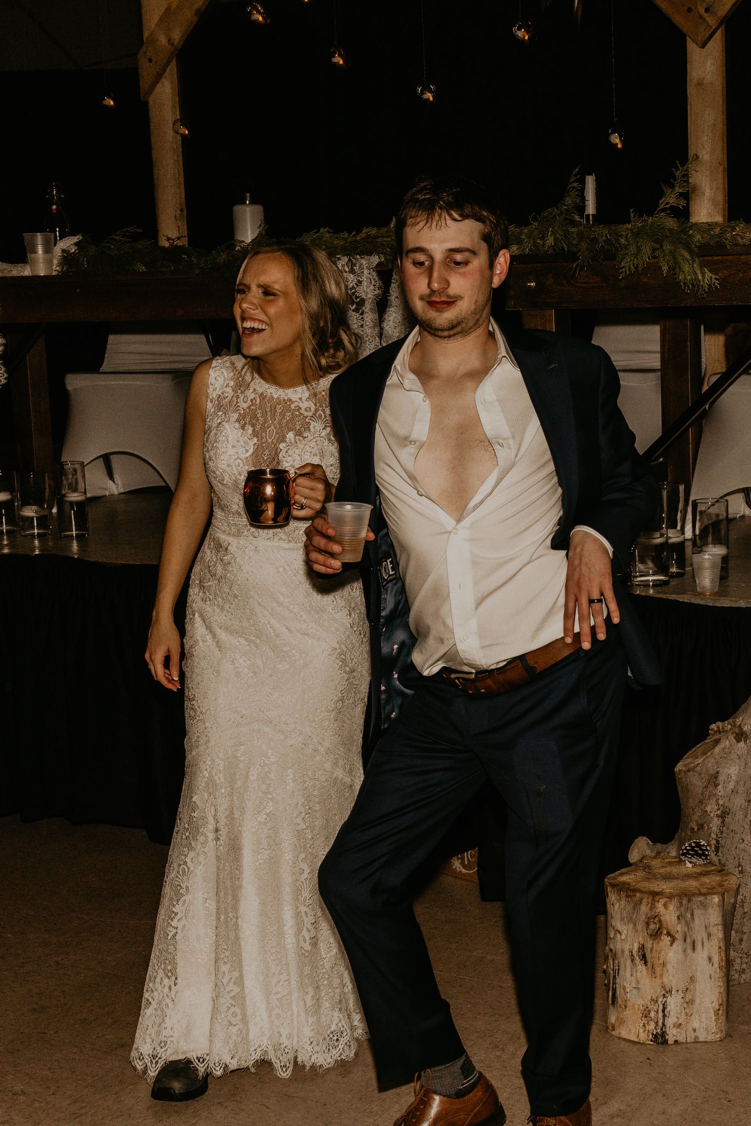 Bride and groom in wedding attire casually dancing with drinks in hand.