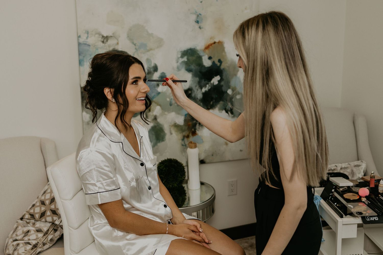 Professional makeup artist applying cosmetics to a client in a white robe during pre-wedding preparations.