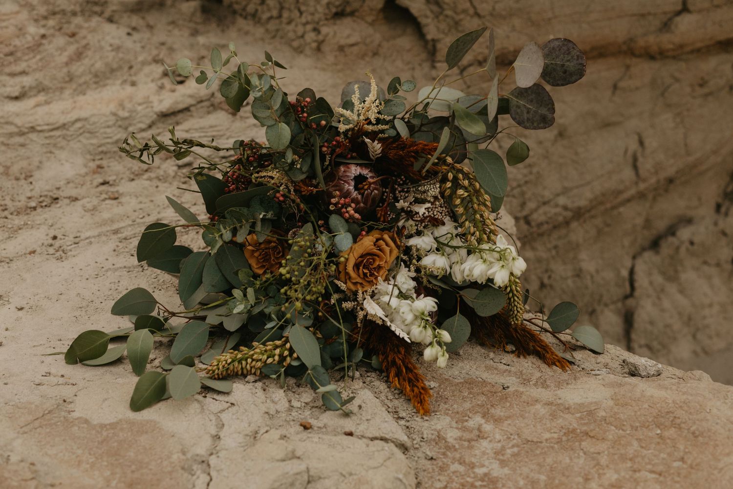 A rustic wedding bouquet featuring eucalyptus, wildflowers and autumn colors placed on textured stone.