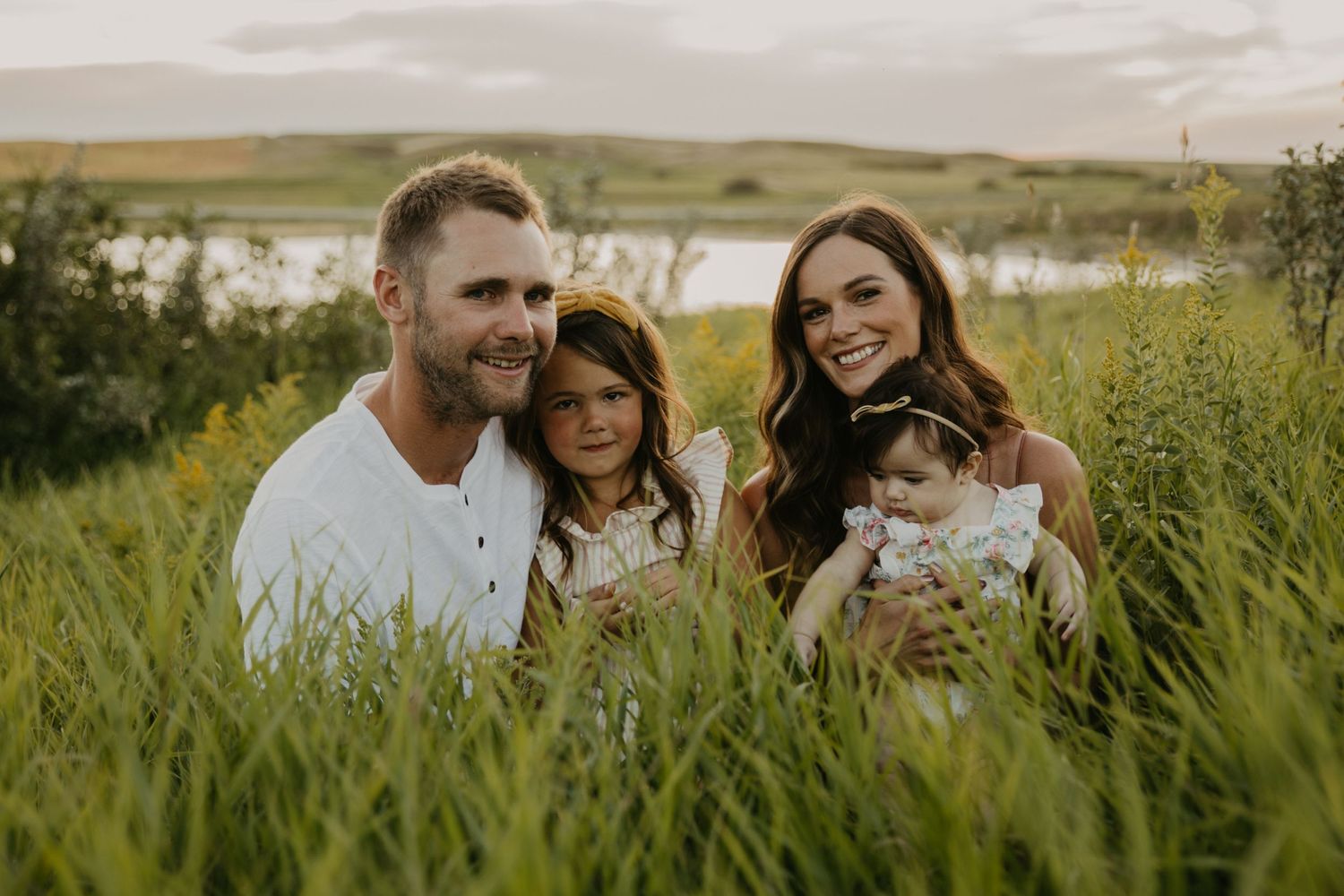 Family portrait in wild grass field with water and rolling hills in background.