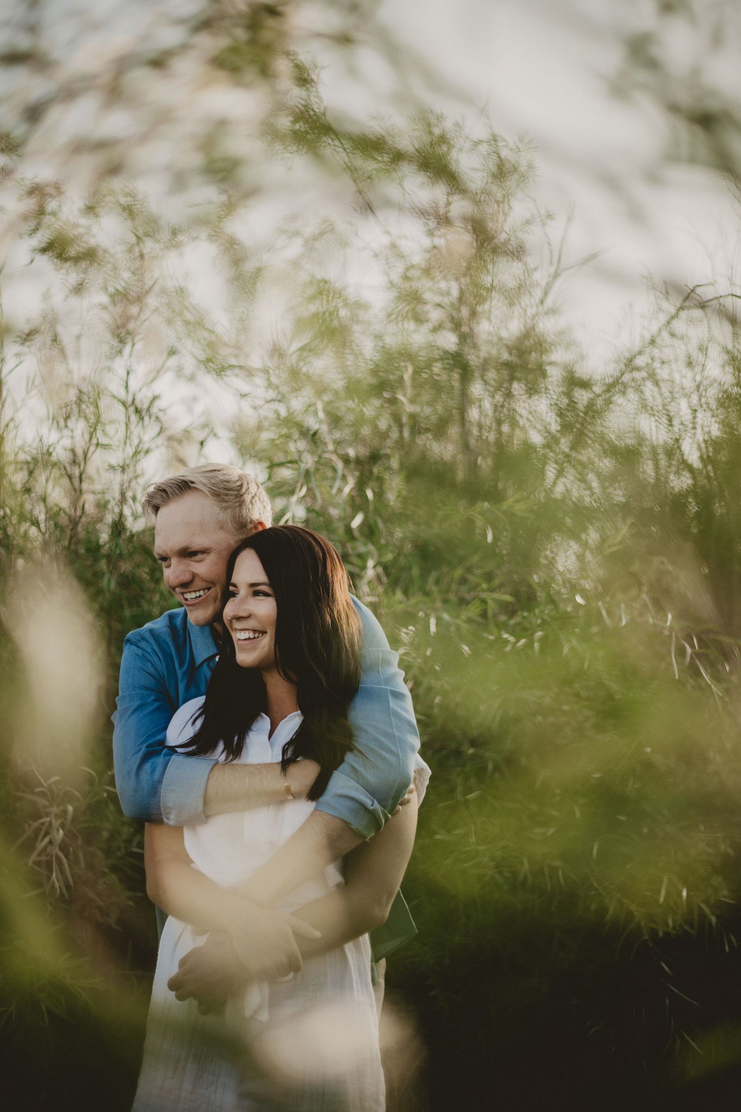 Intimate outdoor portrait of a couple embracing among soft green foliage.