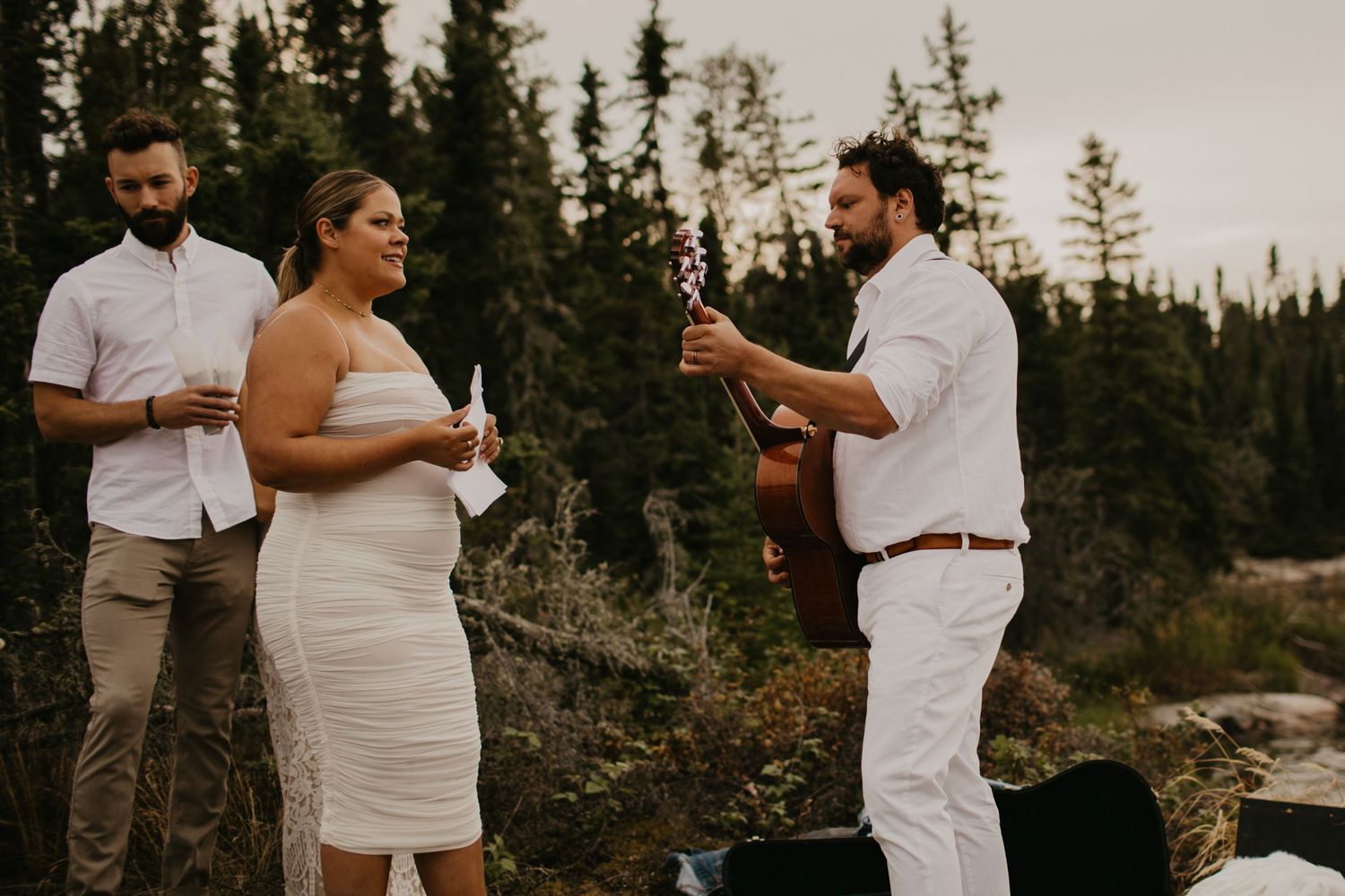 Small wedding celebration gathering on rocky lakeside surrounded by pine trees.