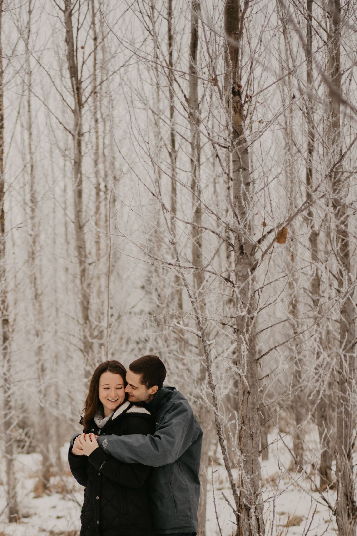 Couple embracing in a snowy winter forest with bare trees.