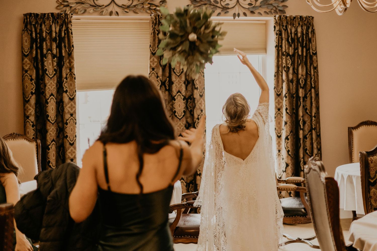 An elegant bride in a lace gown stands with a bridesmaid in a dark dress during a wedding celebration.