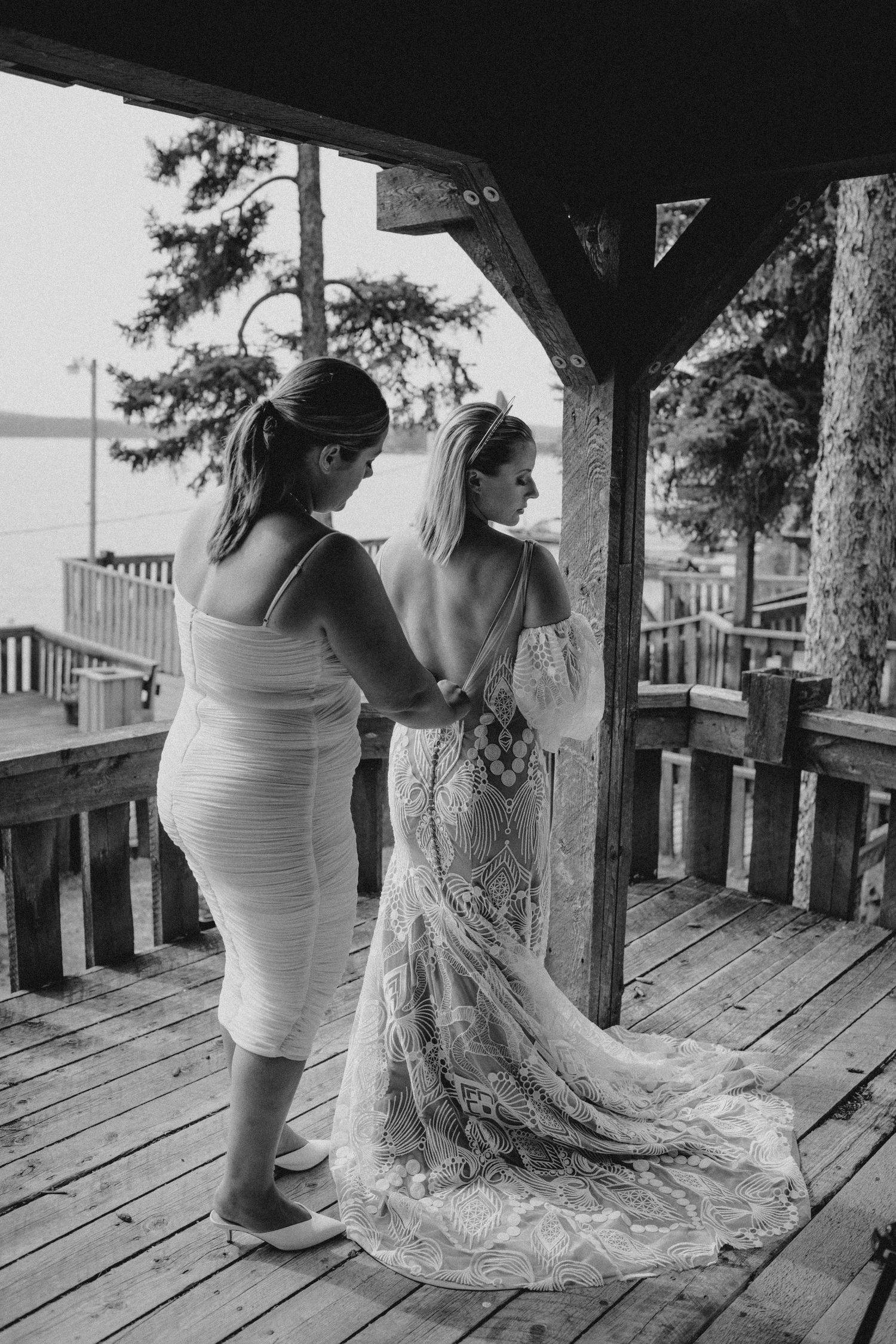 Wedding preparation moment on lakeside deck with flowing lace dress.