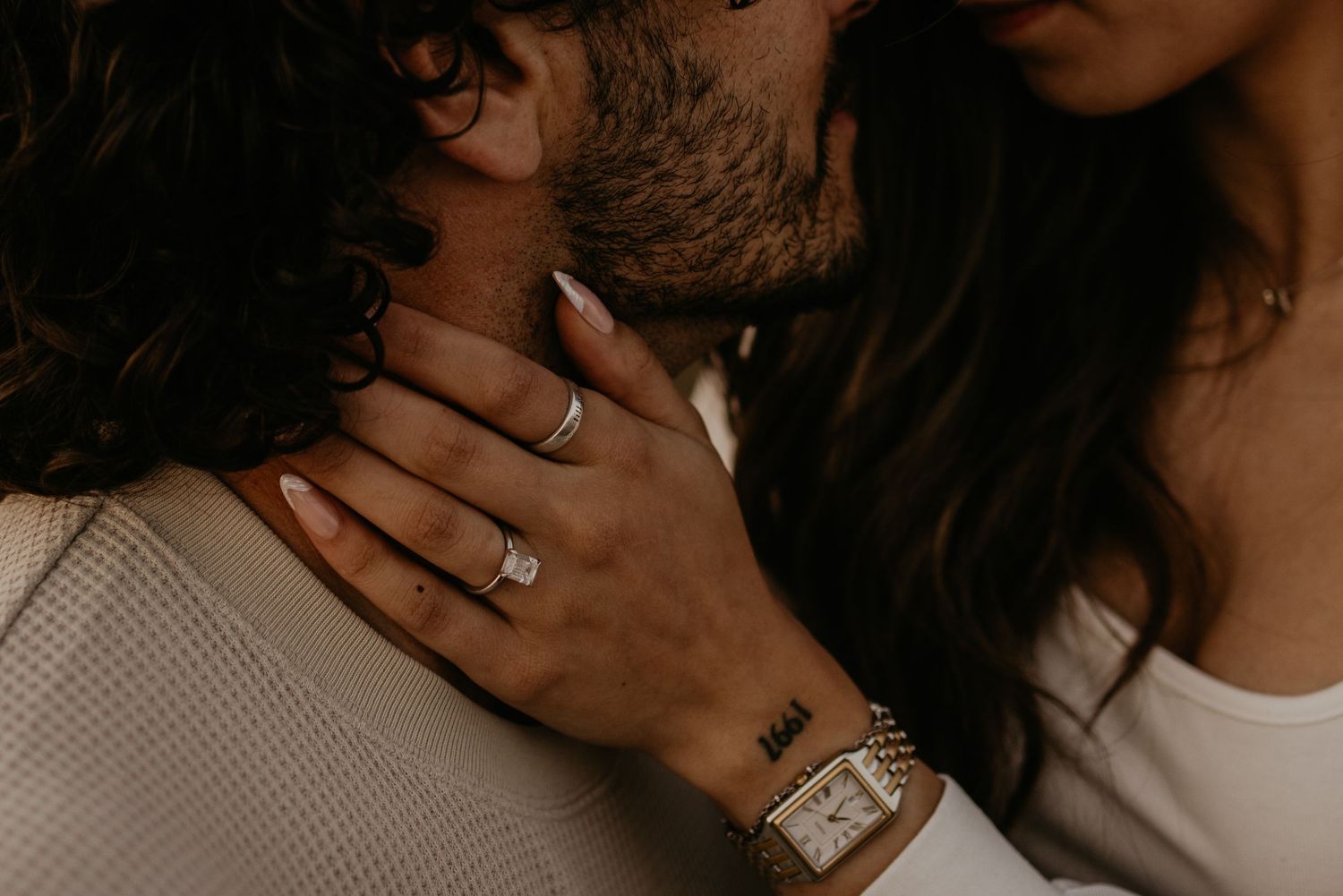 Close-up of intertwined hands with engagement rings in warm, moody lighting.