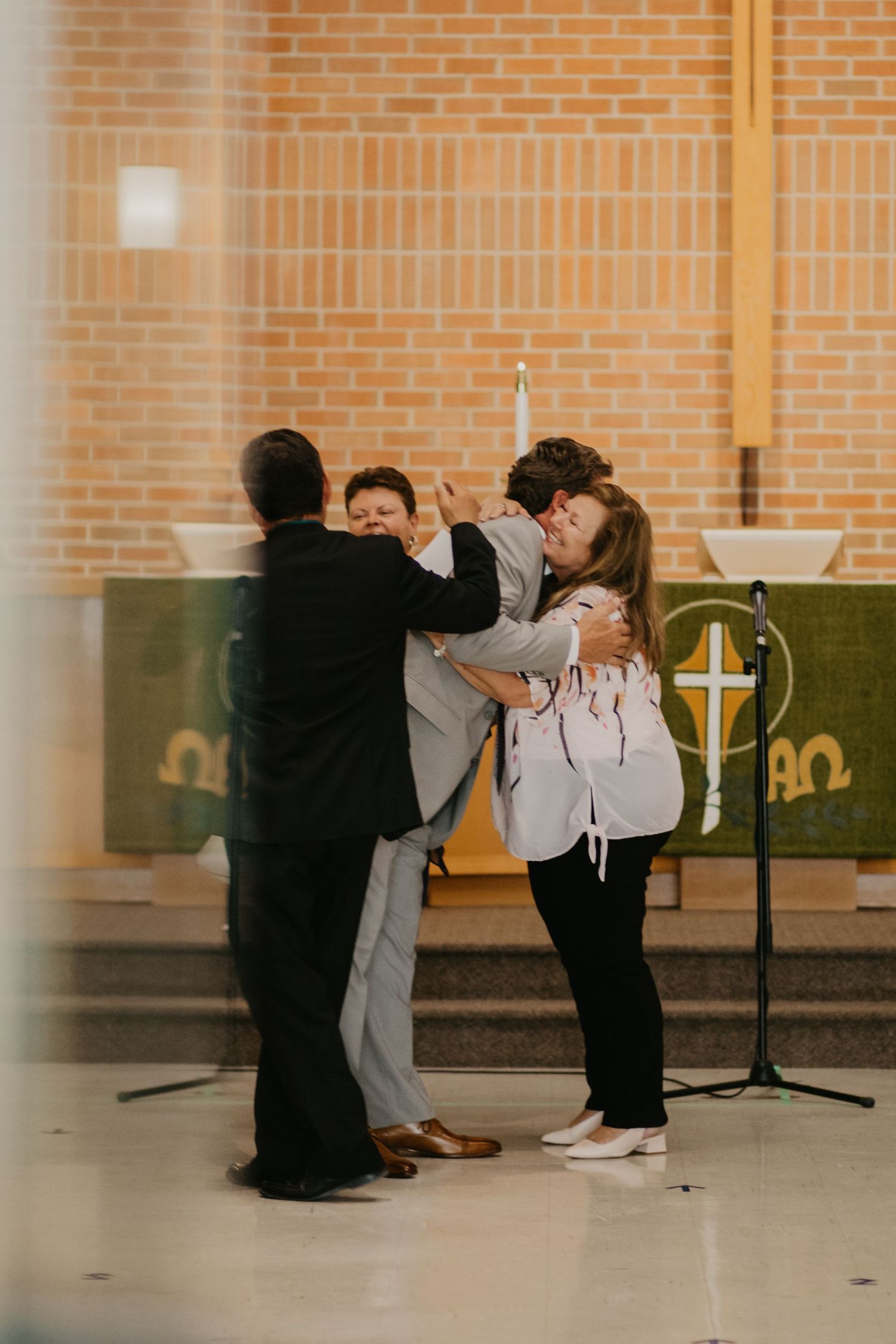 Emotional group hug during indoor church ceremony with brick wall background.