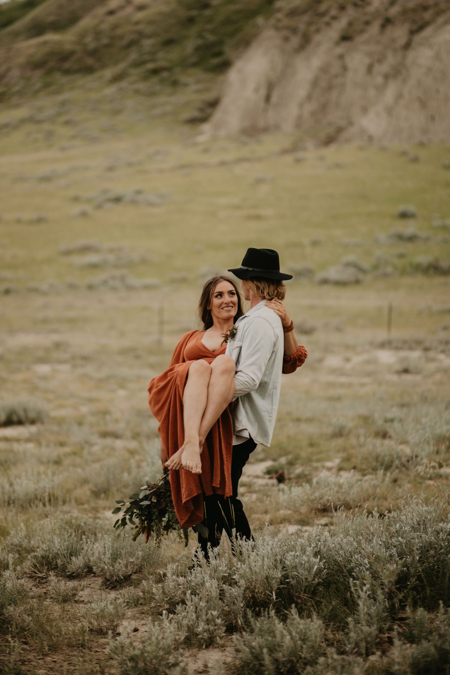 A romantic desert photoshoot with flowing rust-colored dress against dramatic mountain backdrop.