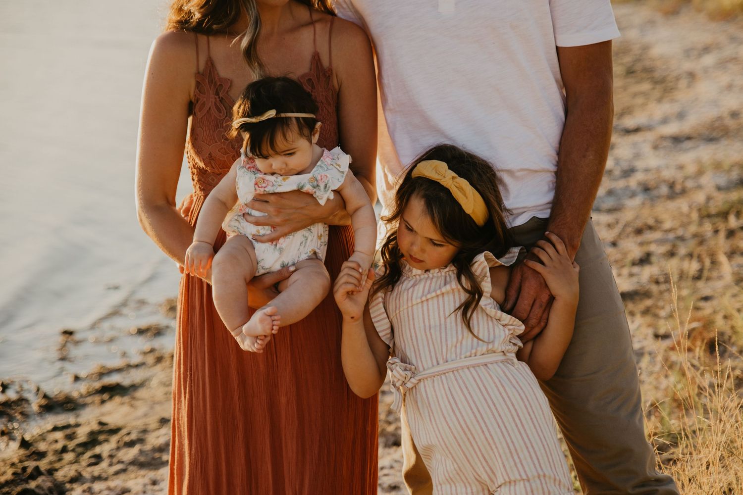 Family in coordinated outfits standing together on a beach at golden hour.