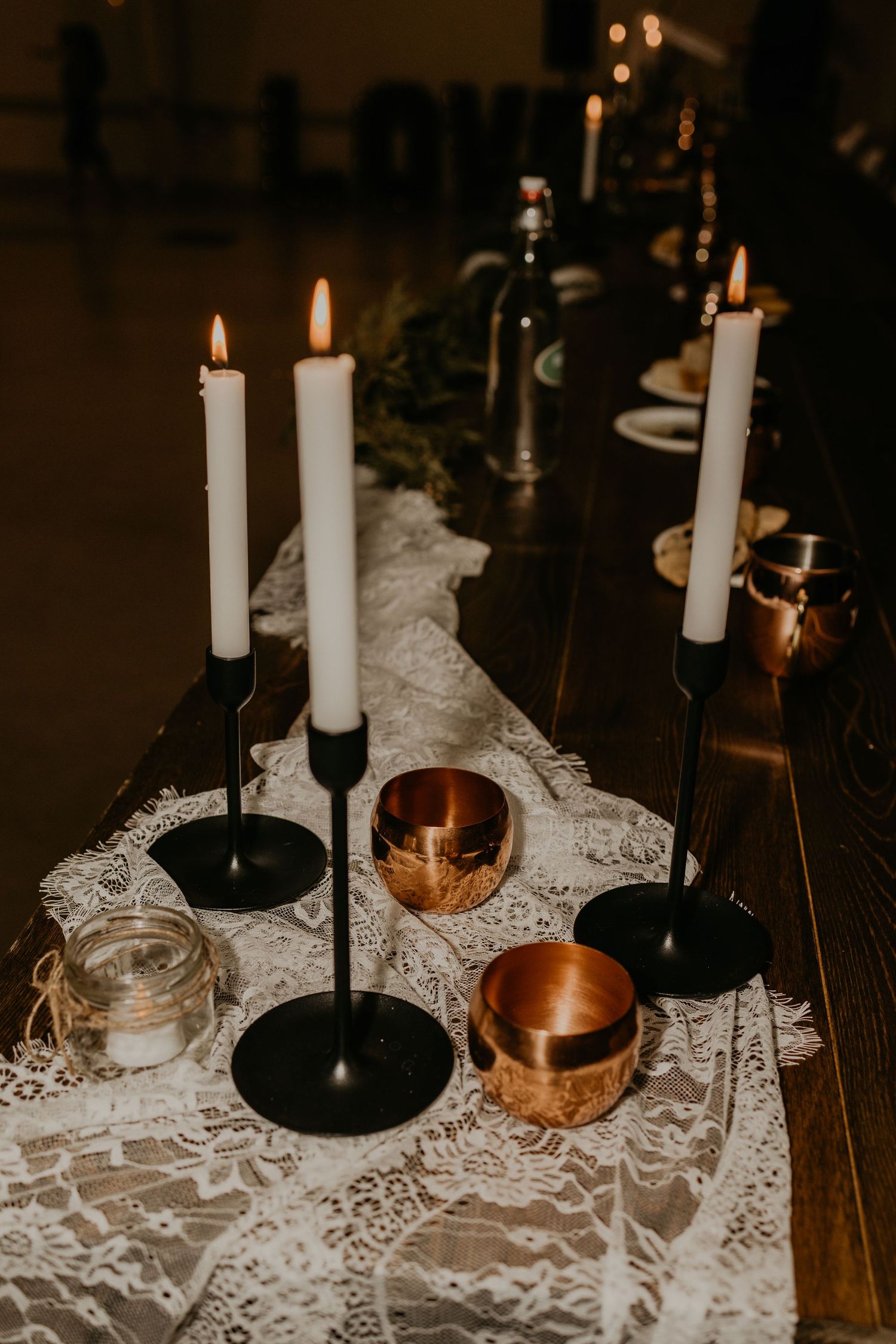 White taper candles in black holders arranged on lace runner with copper accents.