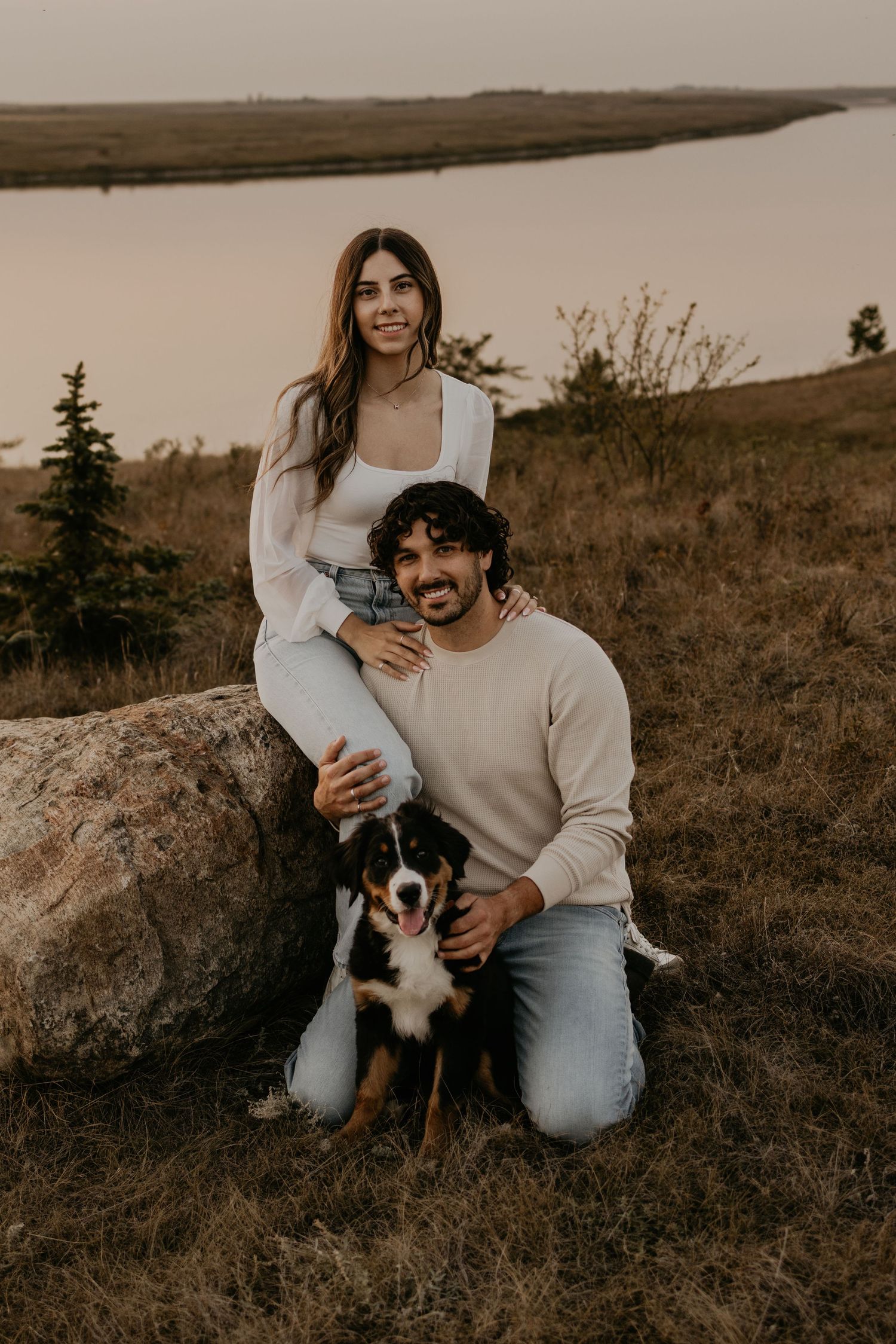 Couple with their small dog enjoying a warm sunset on a rocky hill in a rural landscape.