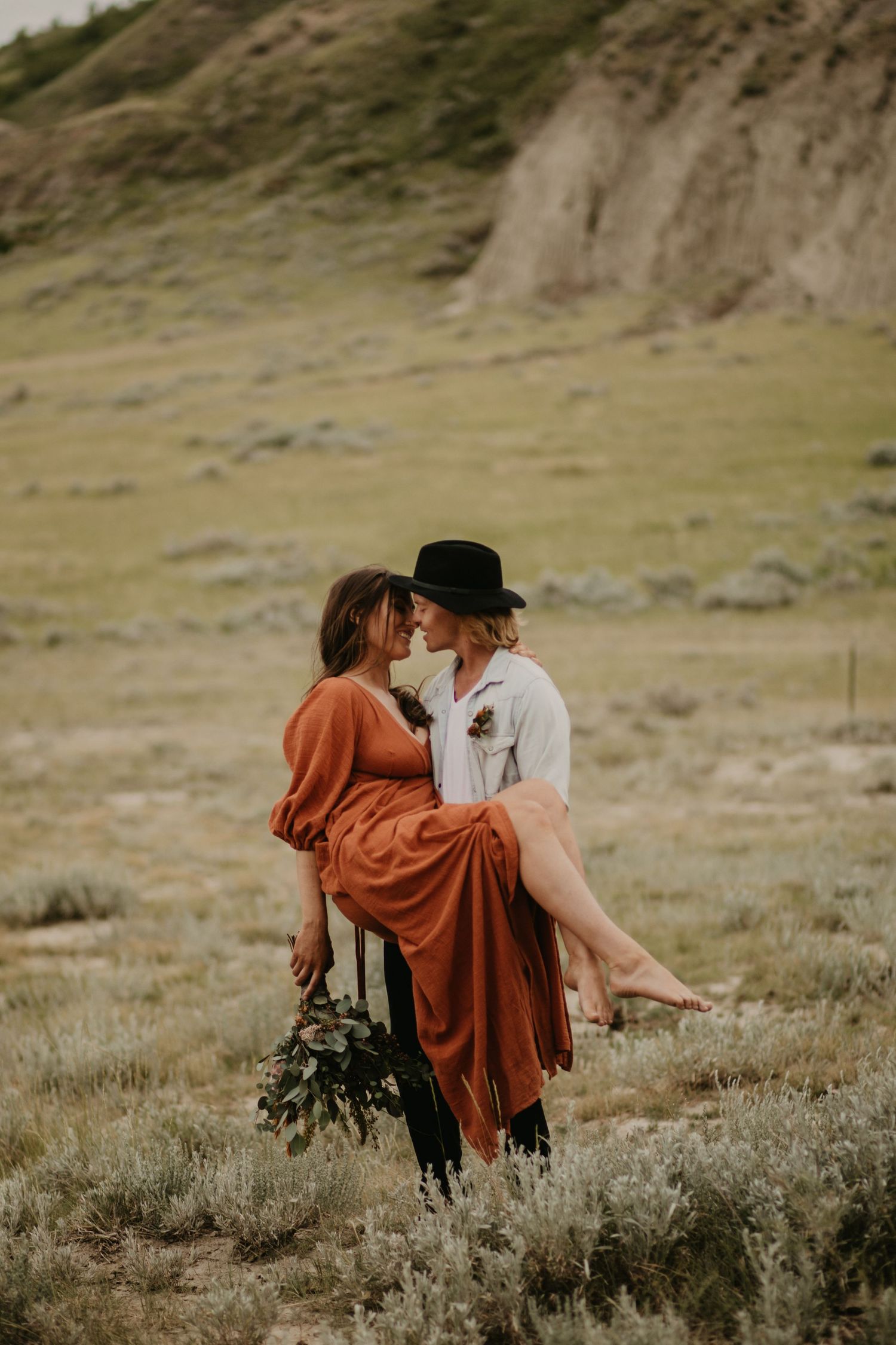Romantic scene with a person in a flowing rust dress being carried in a desert landscape.