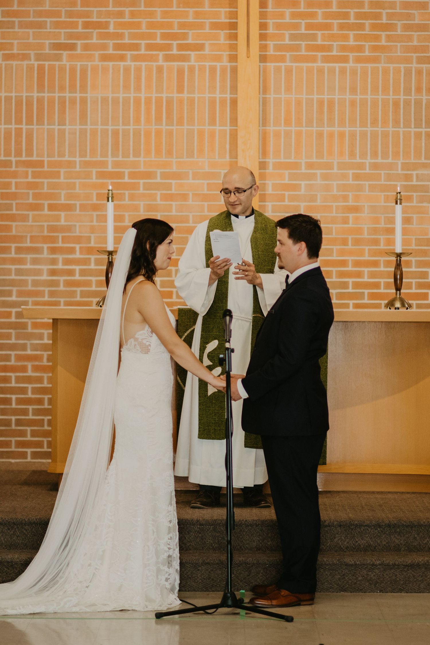 A wedding ceremony in progress at an altar with exposed brick walls and two white candles.