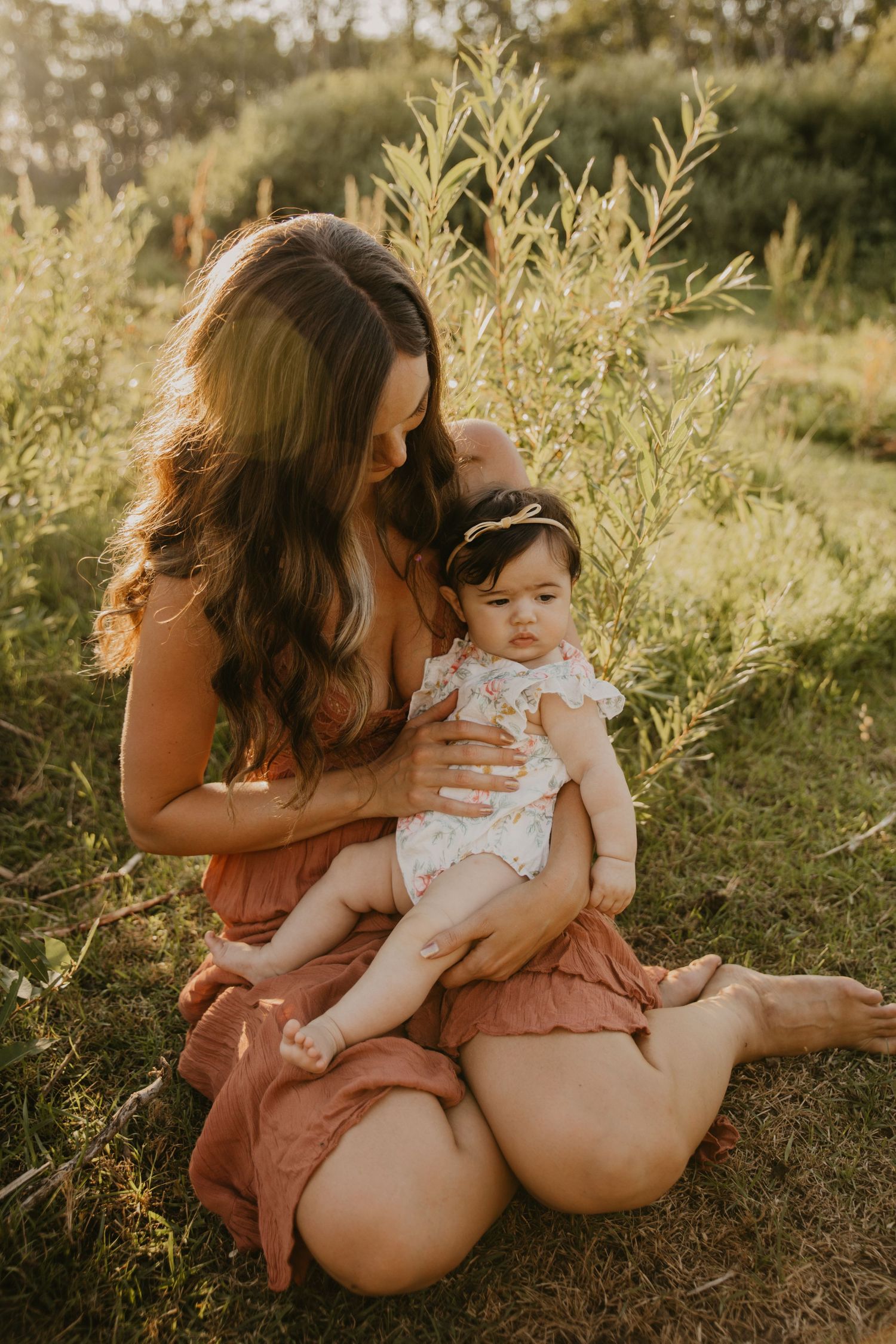 A tender family moment captured in golden sunlight among olive branches and tall grass.