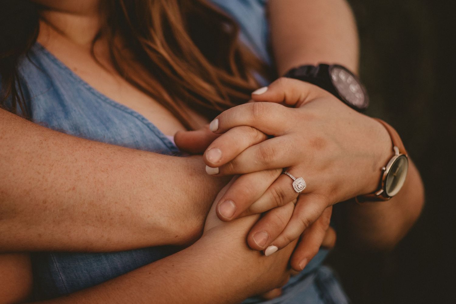 Close-up shot of hands with engagement ring intertwined in warm light.