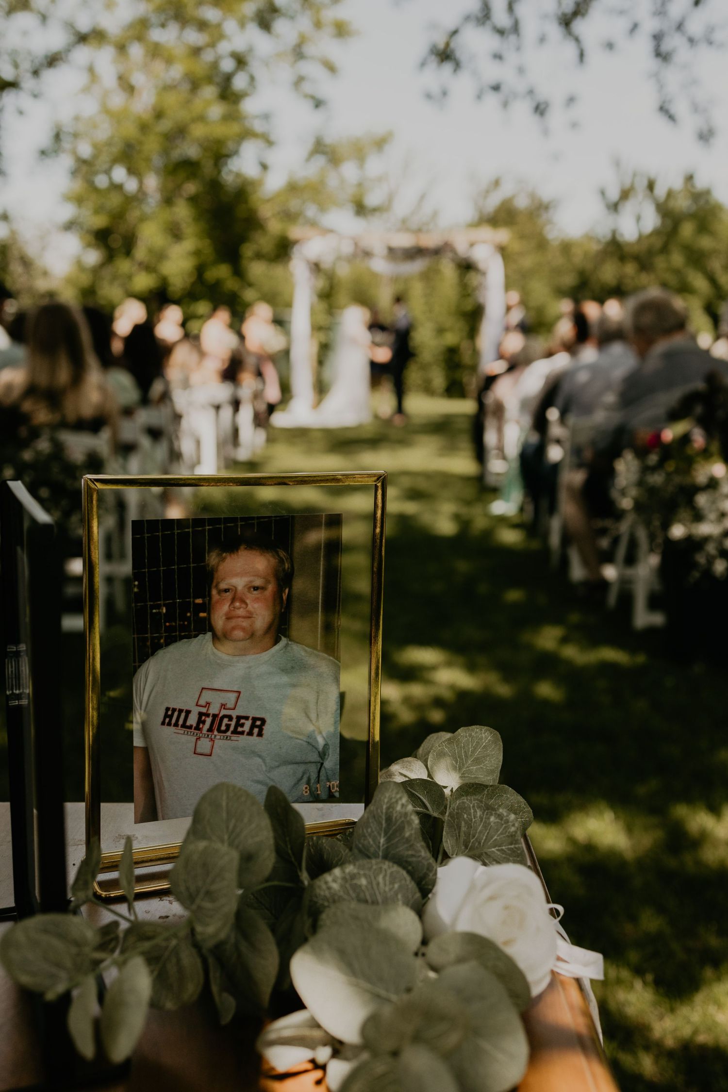 Memorial photo display with flowers at an outdoor wedding ceremony.