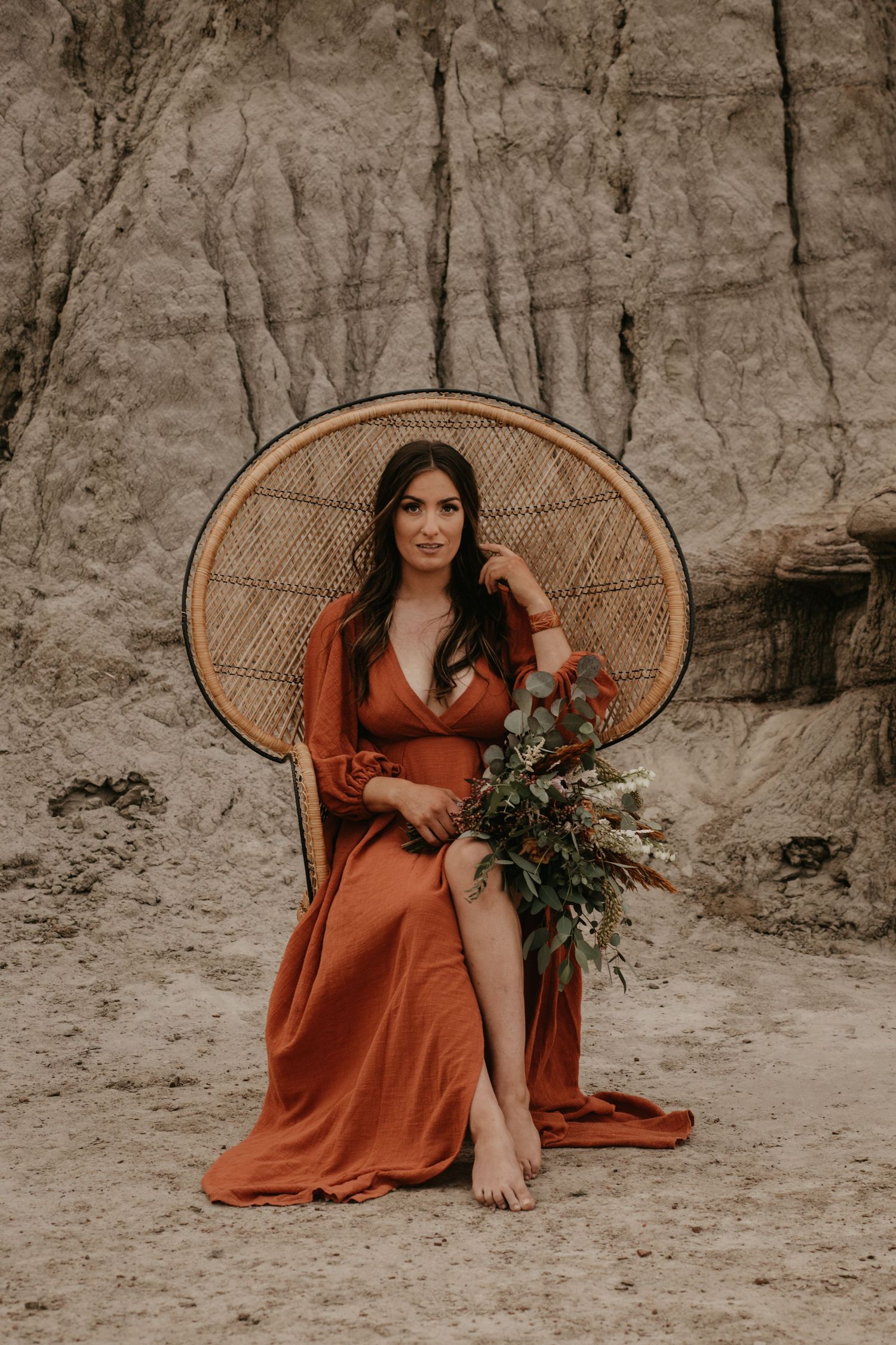 A woman in a rust-colored dress sits on a peacock chair against limestone cliffs.