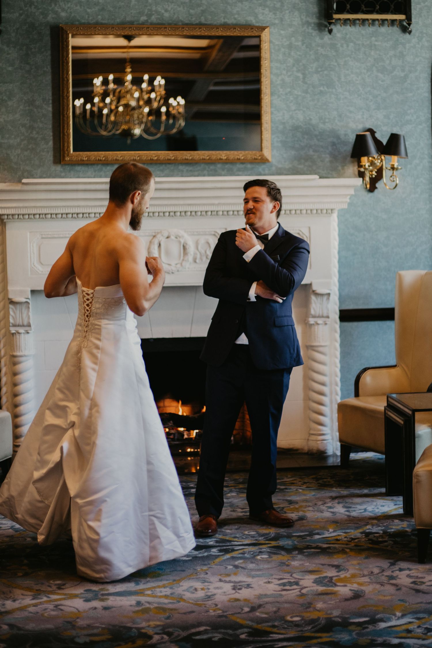 A heartwarming wedding moment in front of a classic white fireplace with an ornate mirror above.