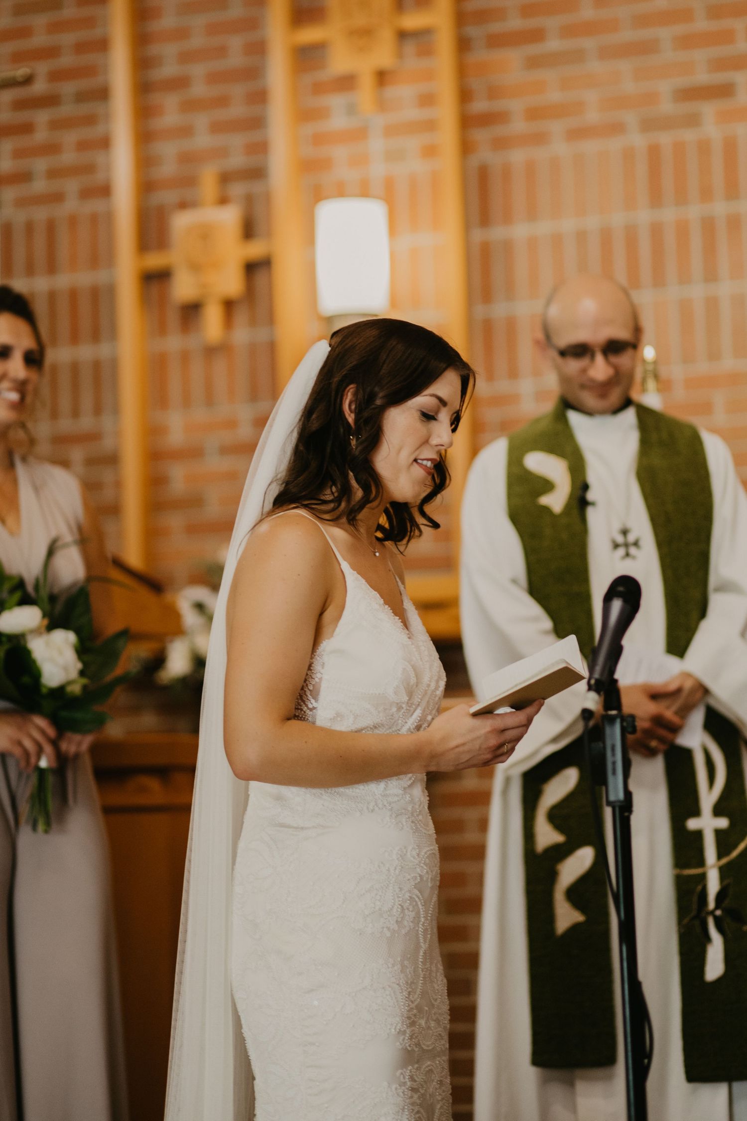 A bride reads from a paper during her wedding ceremony in a brick church.