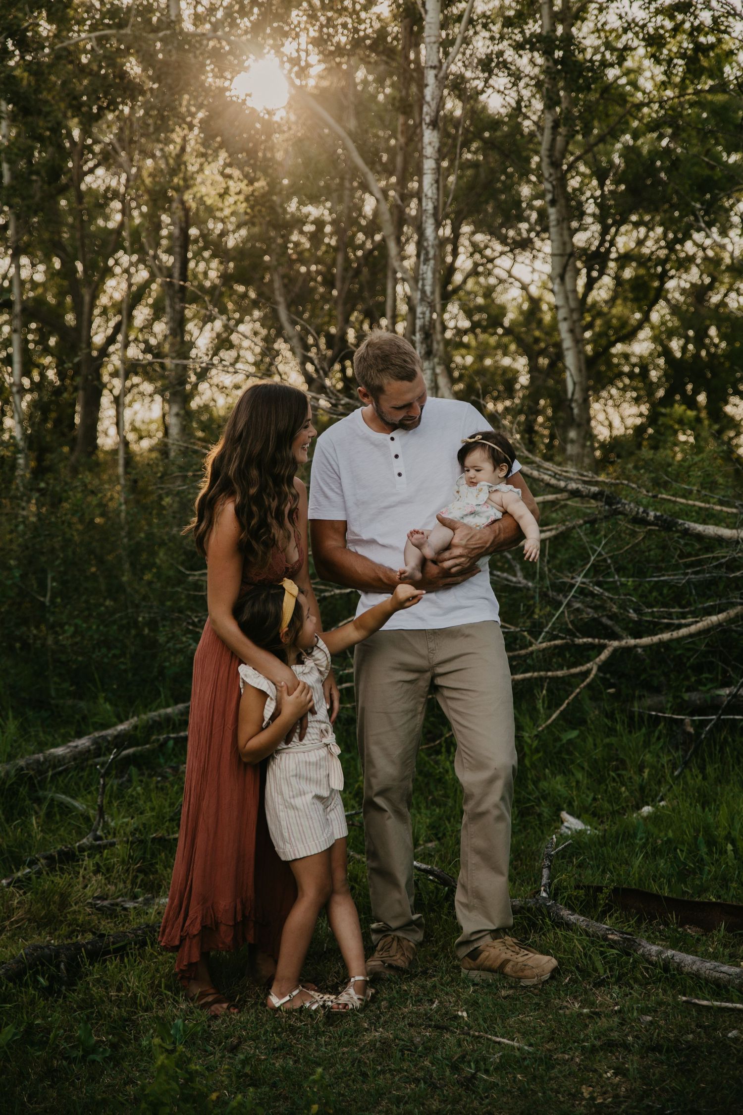 Family gathering in wooded area during golden hour with sunlight filtering through trees.