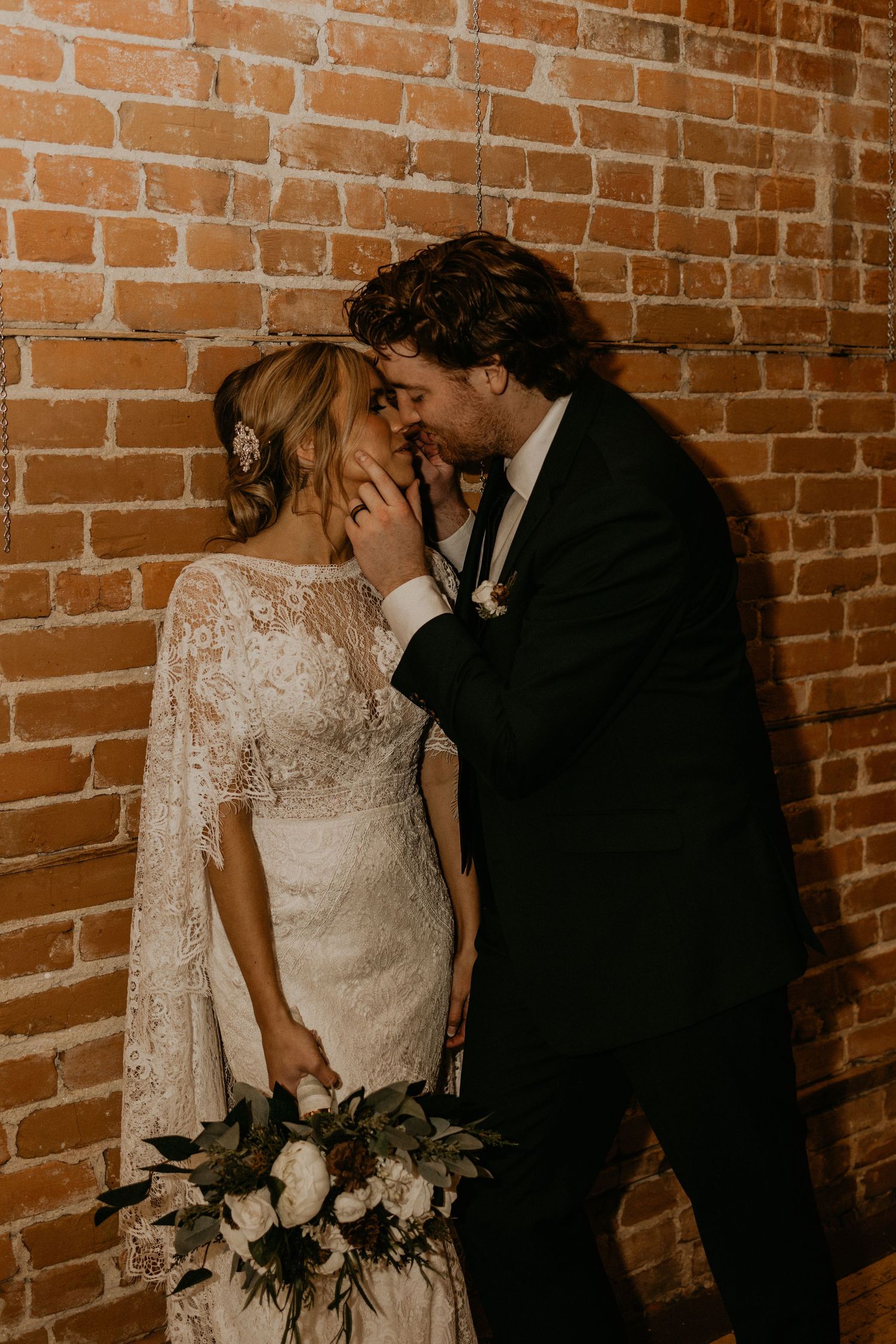 Intimate wedding moment captured against brick wall with bridal bouquet of white flowers.