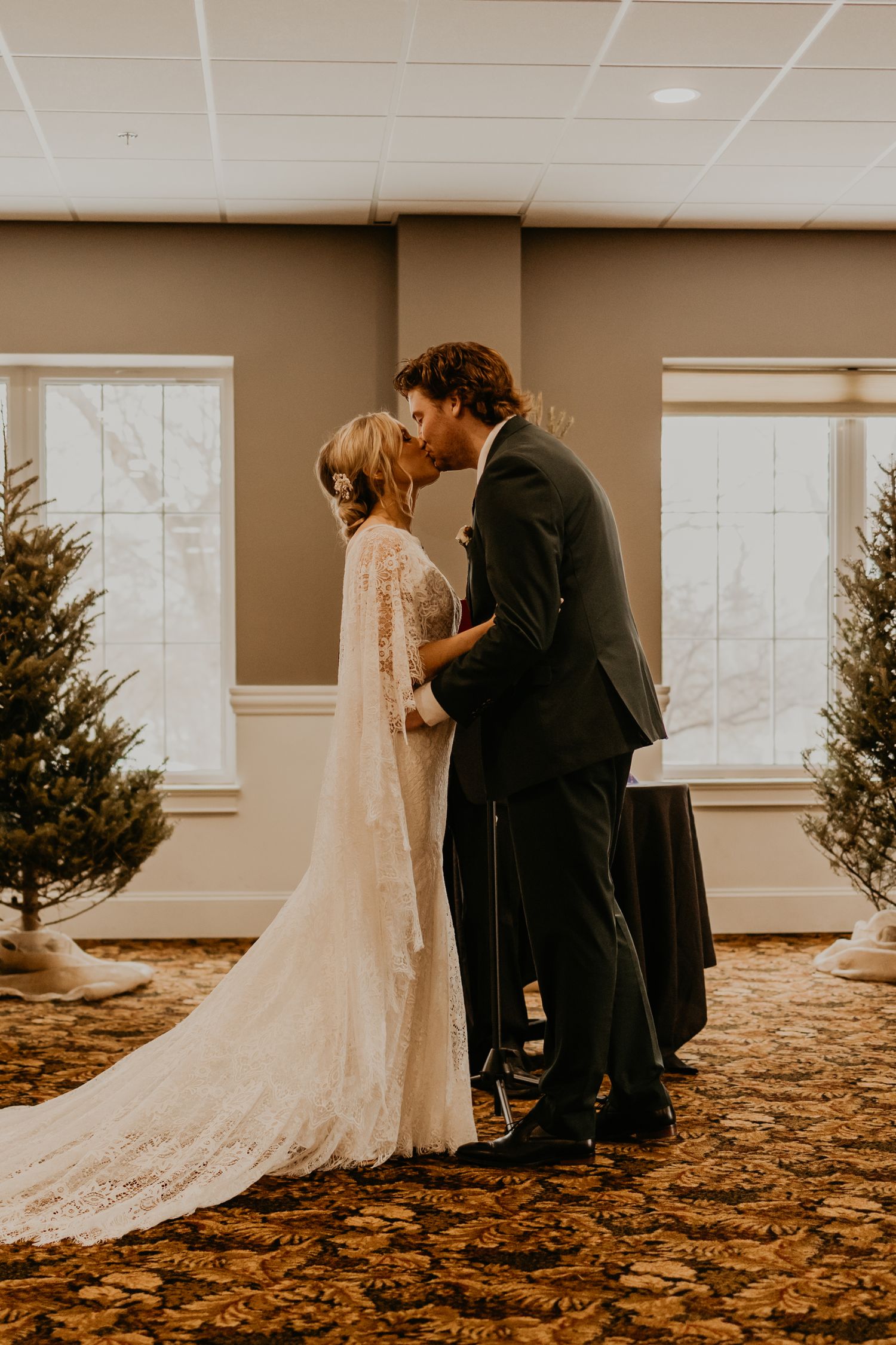Romantic wedding kiss in venue decorated with Christmas trees.