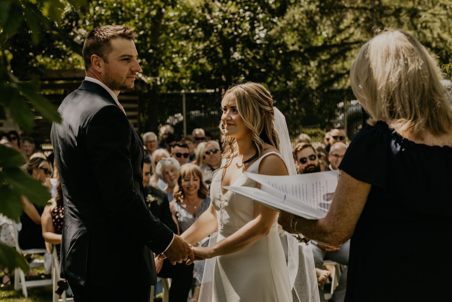 Outdoor garden wedding ceremony with couple exchanging vows under trees.