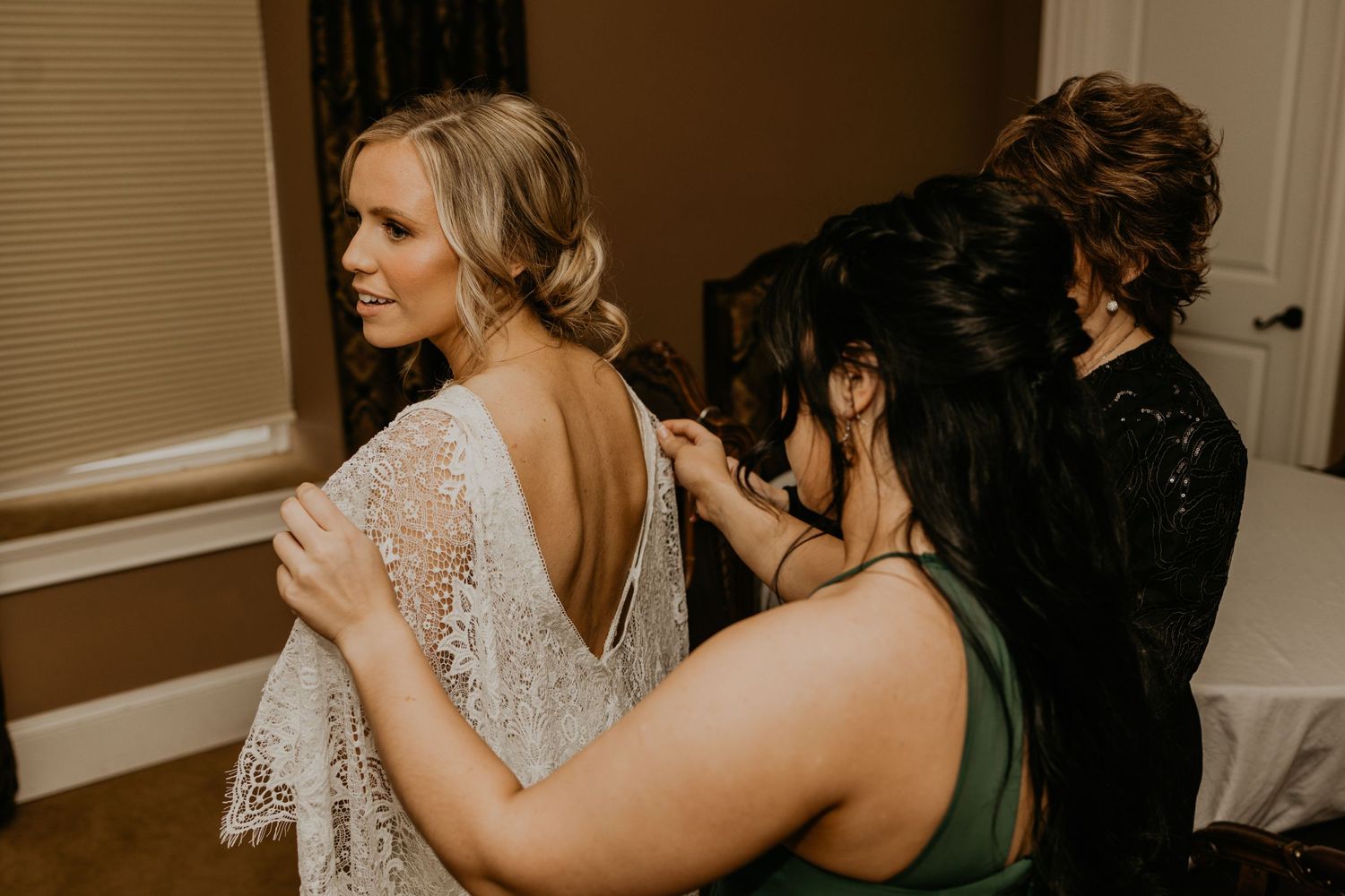 Multiple people helping adjust a bride's lace wedding dress during preparation.
