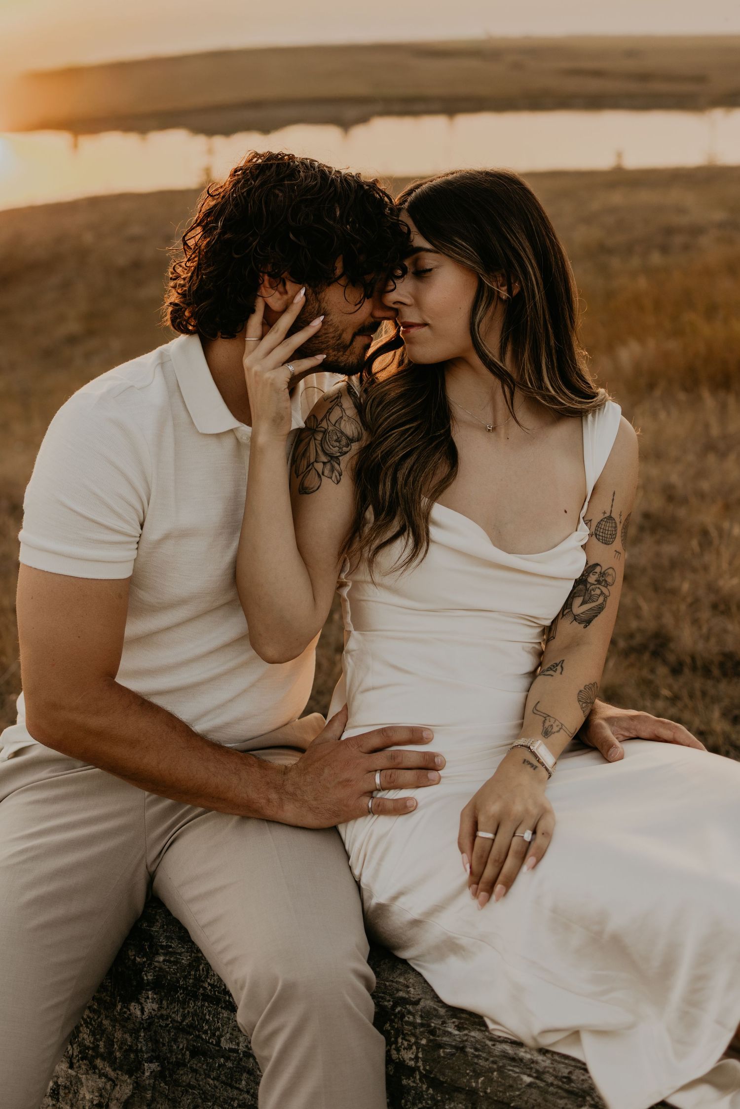An intimate moment between a couple in white attire against a sunset backdrop.