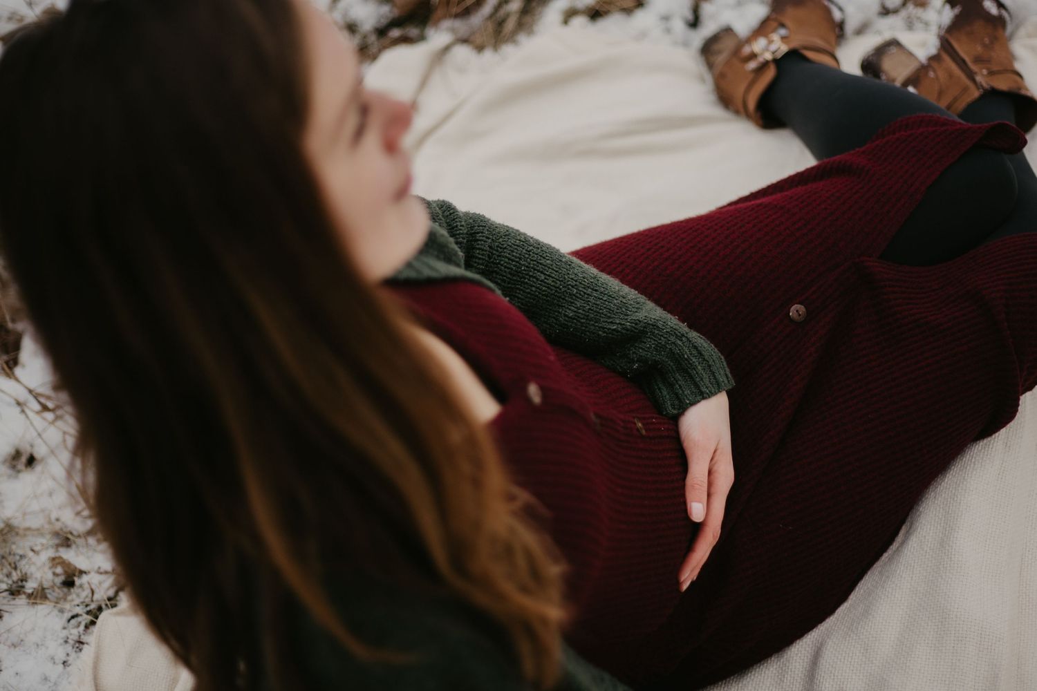 A person in winter clothing reclines on snowy ground during a winter photoshoot.