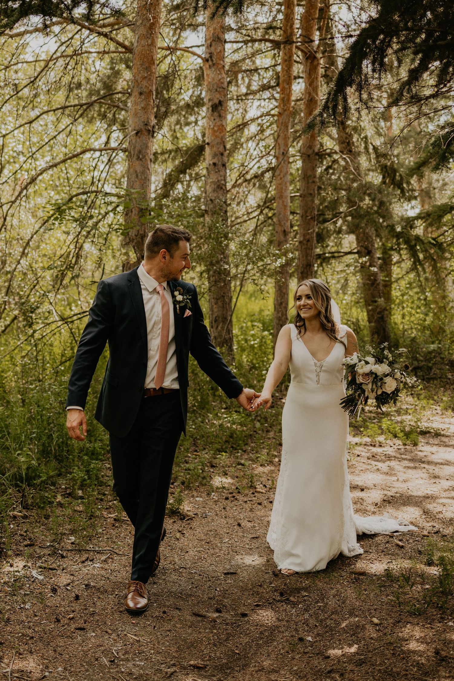 A couple walks hand in hand along a forest trail on their wedding day.