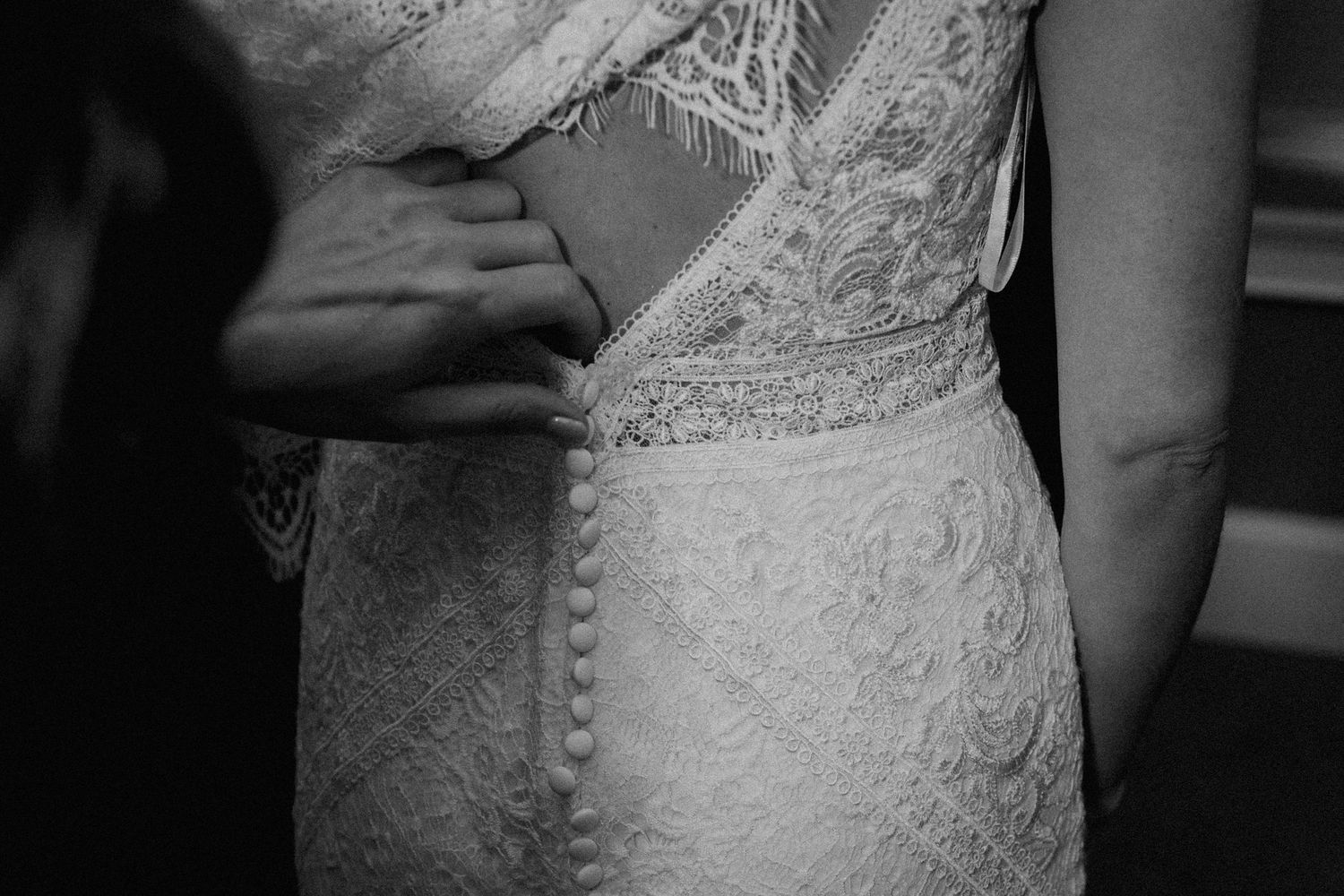 Black and white detail shot of delicate lace buttons on the back of a wedding gown.