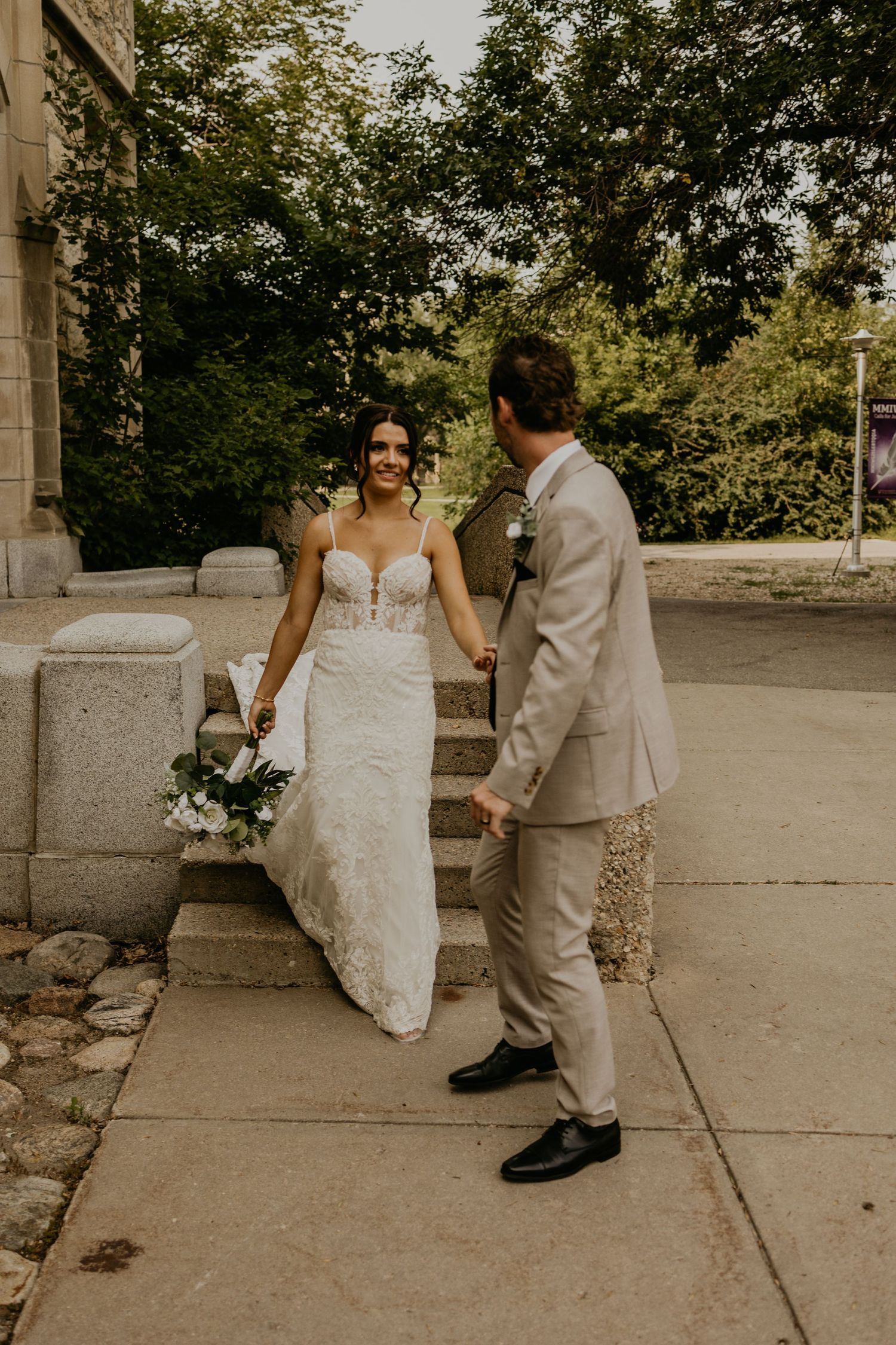 Elegant couple in wedding attire standing by stone building exterior.