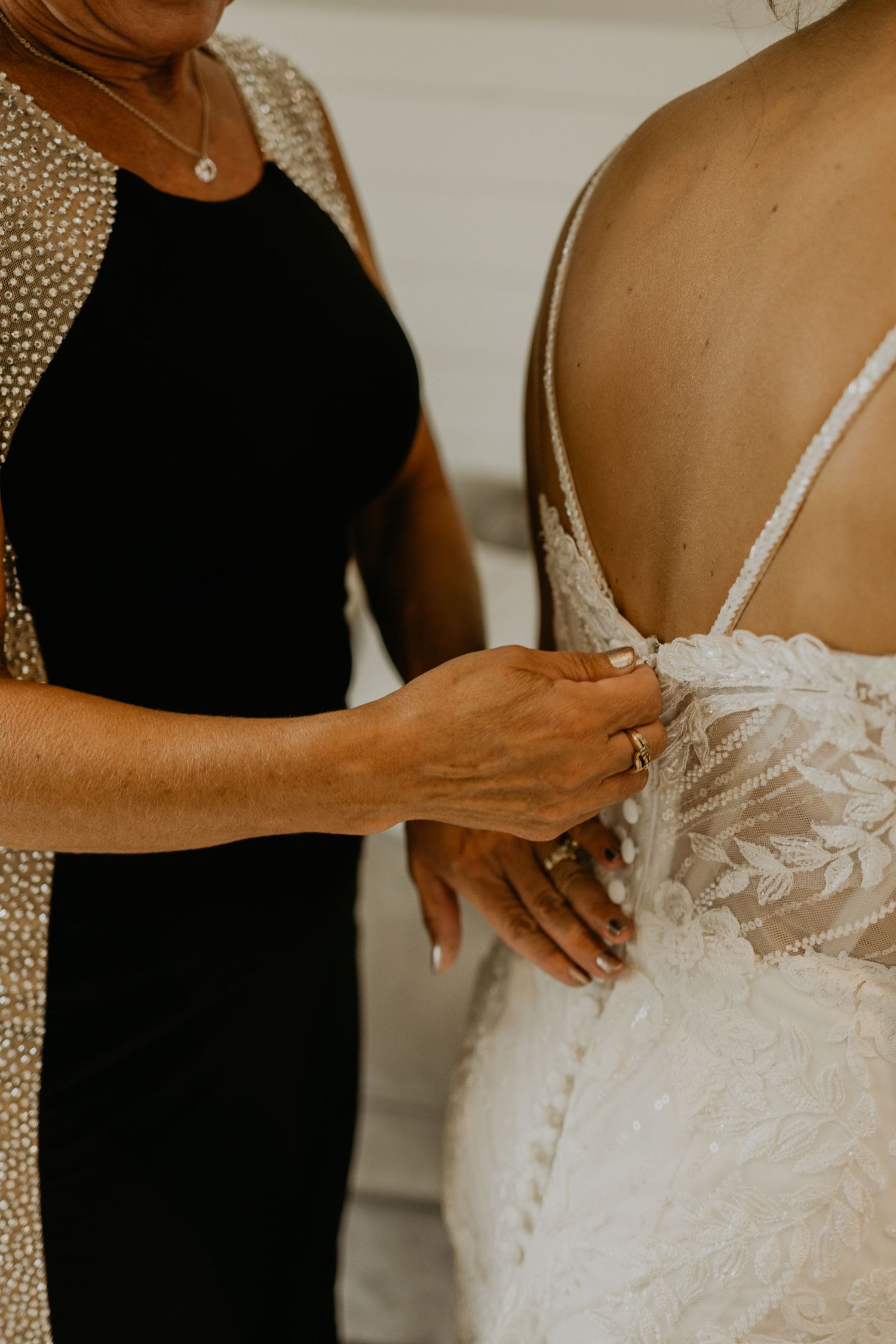 Close-up detail of hands adjusting the back of an intricate lace wedding gown.