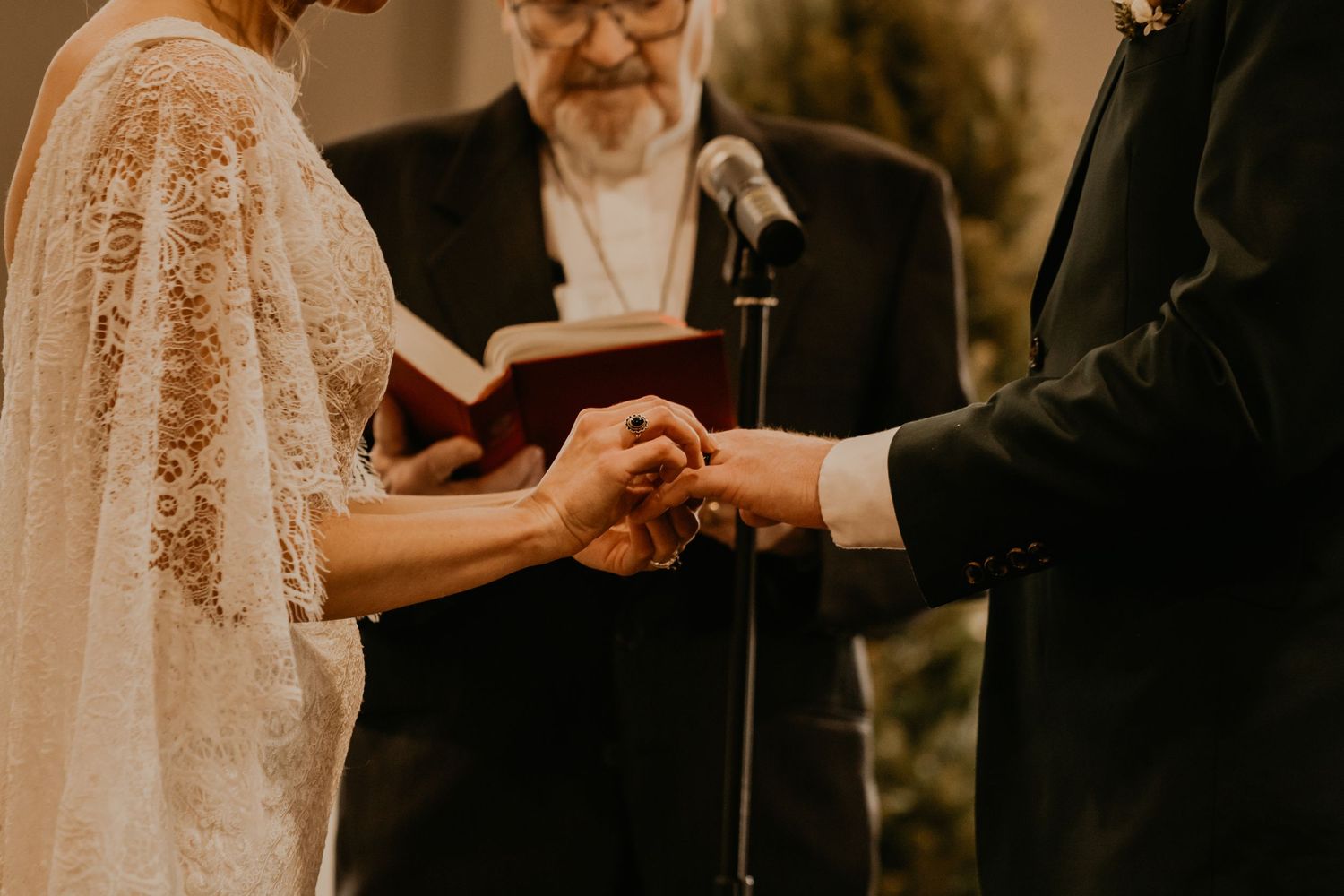 Close-up of wedding ring exchange ceremony with officiant holding ceremony book.