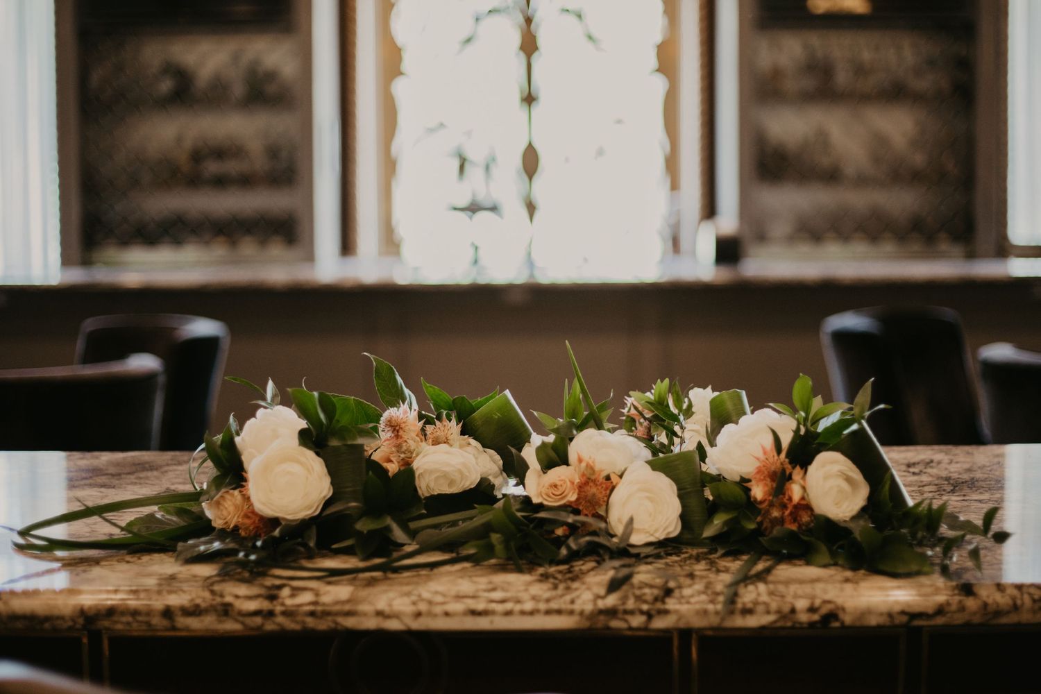 Elegant floral centerpiece with white roses and greenery on rustic wooden table.