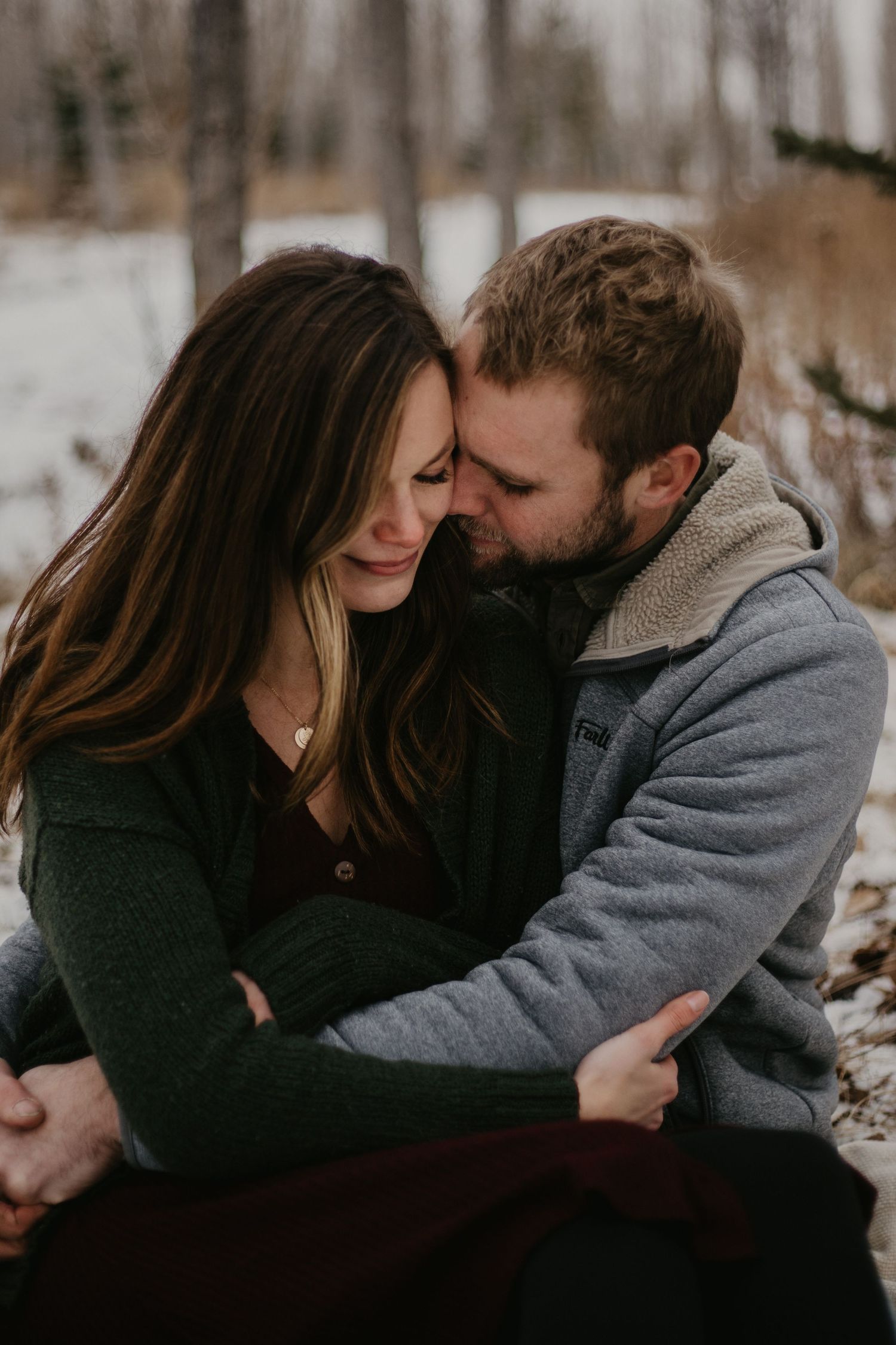 A couple shares a tender moment while embracing outdoors in winter attire.