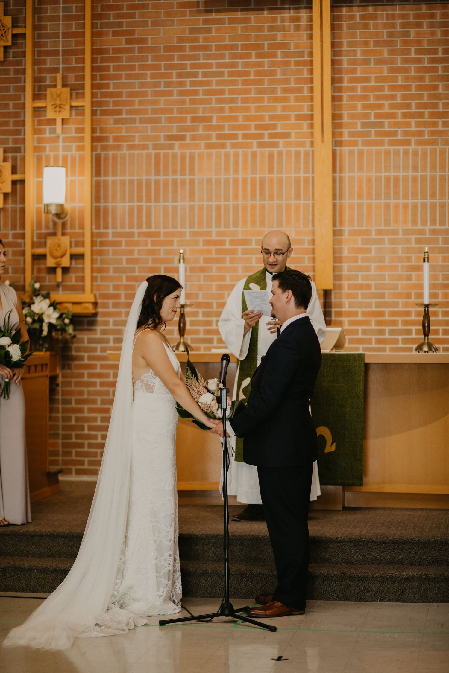 Wedding ceremony in progress inside brick church with wooden cross details and altar candles.