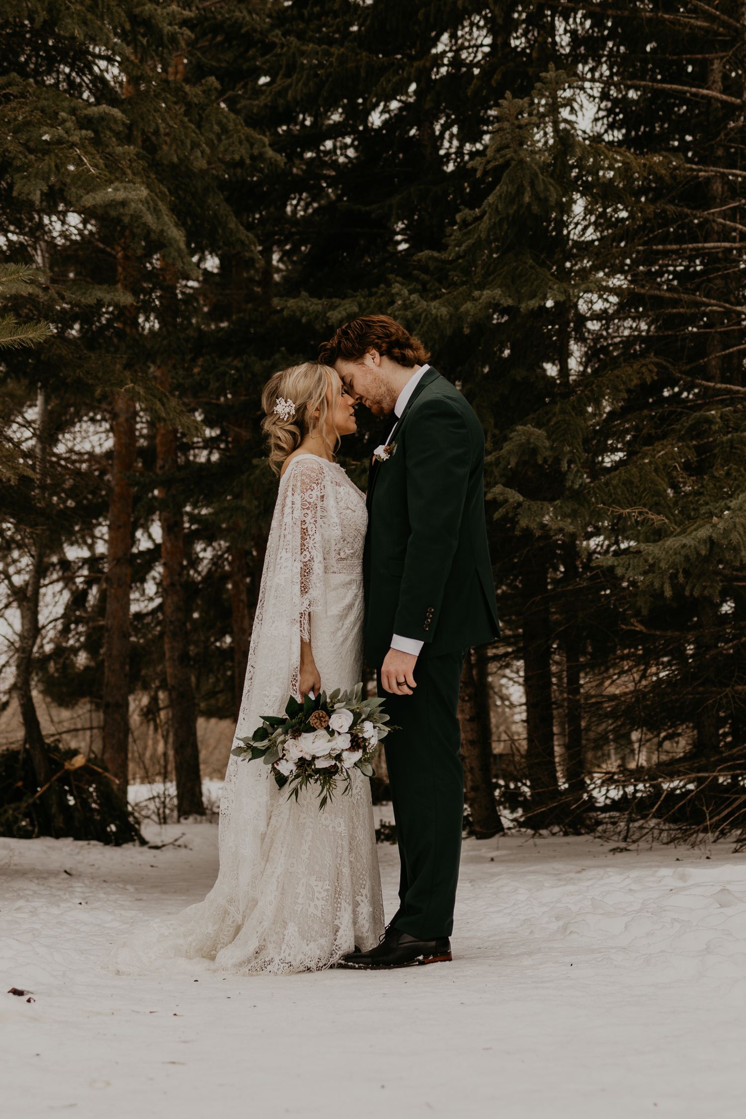 Intimate wedding portrait of a couple standing close together in a snow-covered forest.