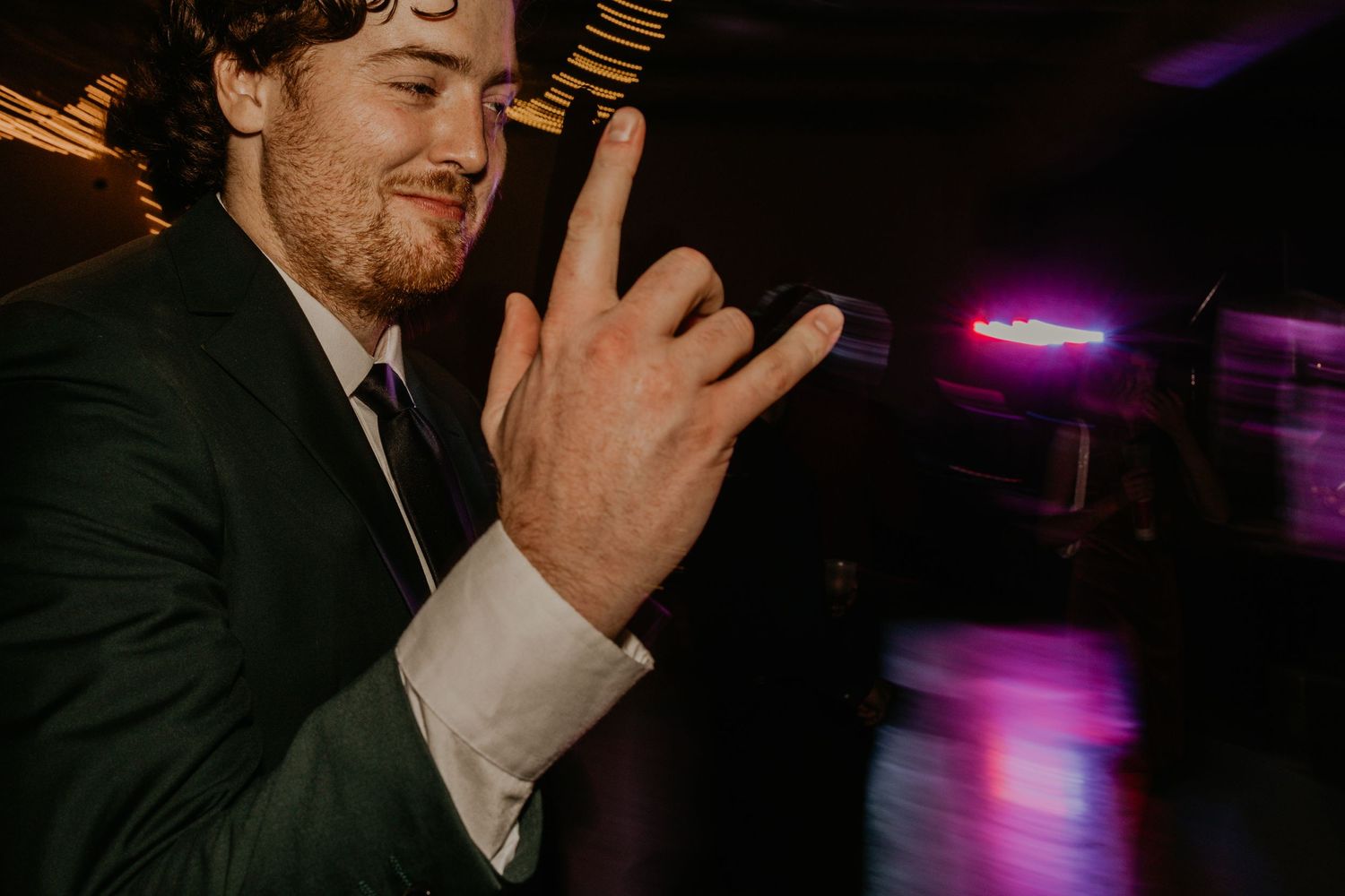 Guest making rock and roll hand gesture at dimly lit wedding reception.